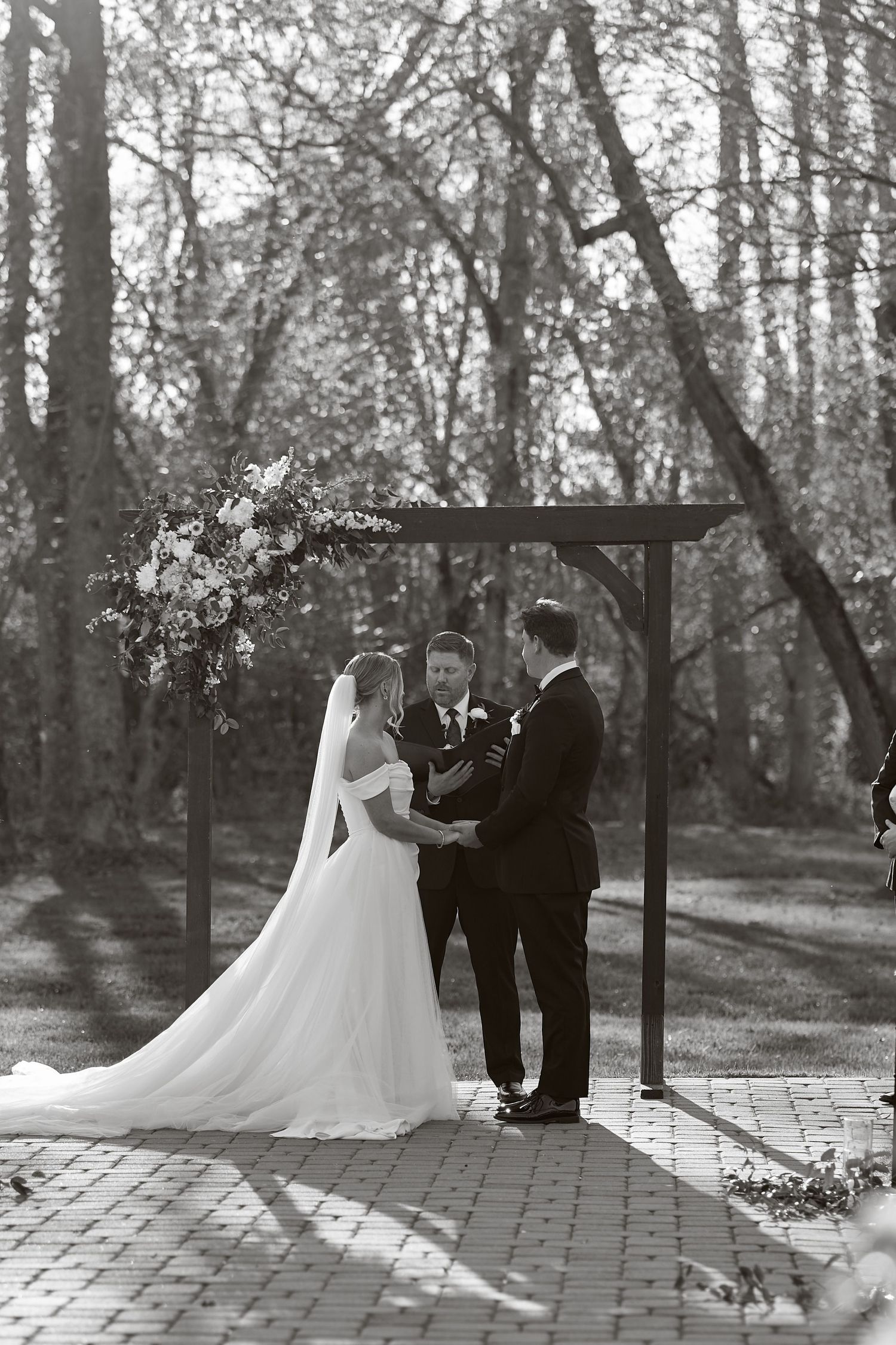 Bride and groom exchange vows under a floral arch in an outdoor woodland wedding ceremony. North Carolina Wedding Photographer.