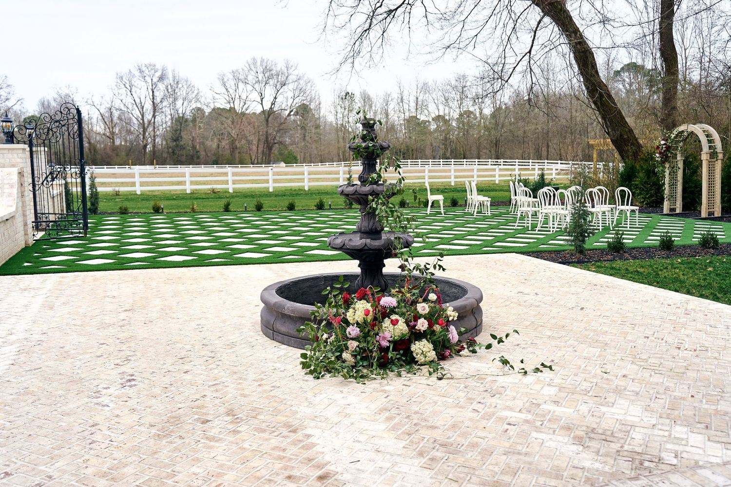 Elegant outdoor event venue with artificial turf lawn, stone patio, and decorative floral fountain centerpiece.