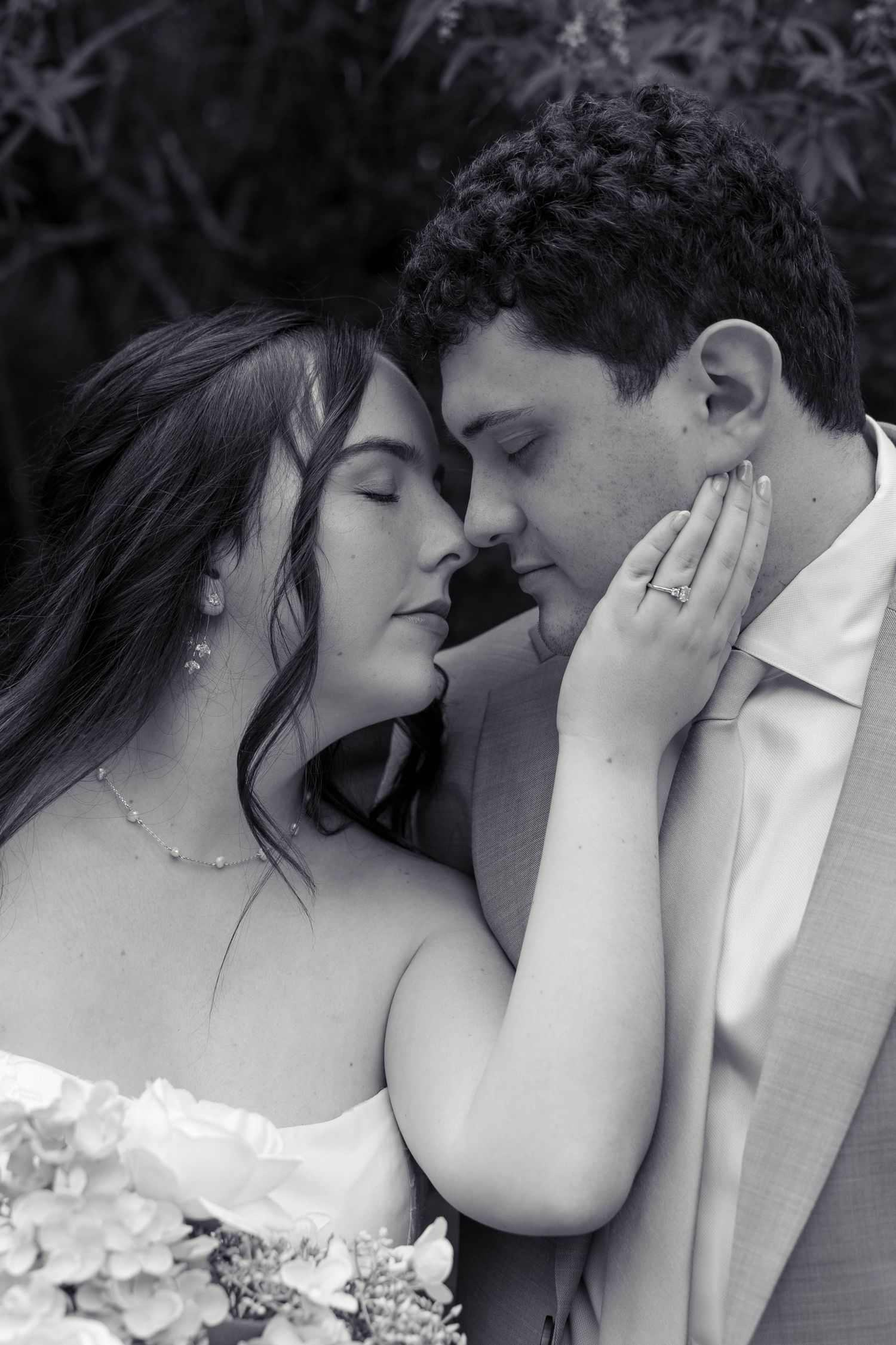 Intimate black and white close-up of bride and groom nearly kissing, bride holding bouquet of hydrangeas.