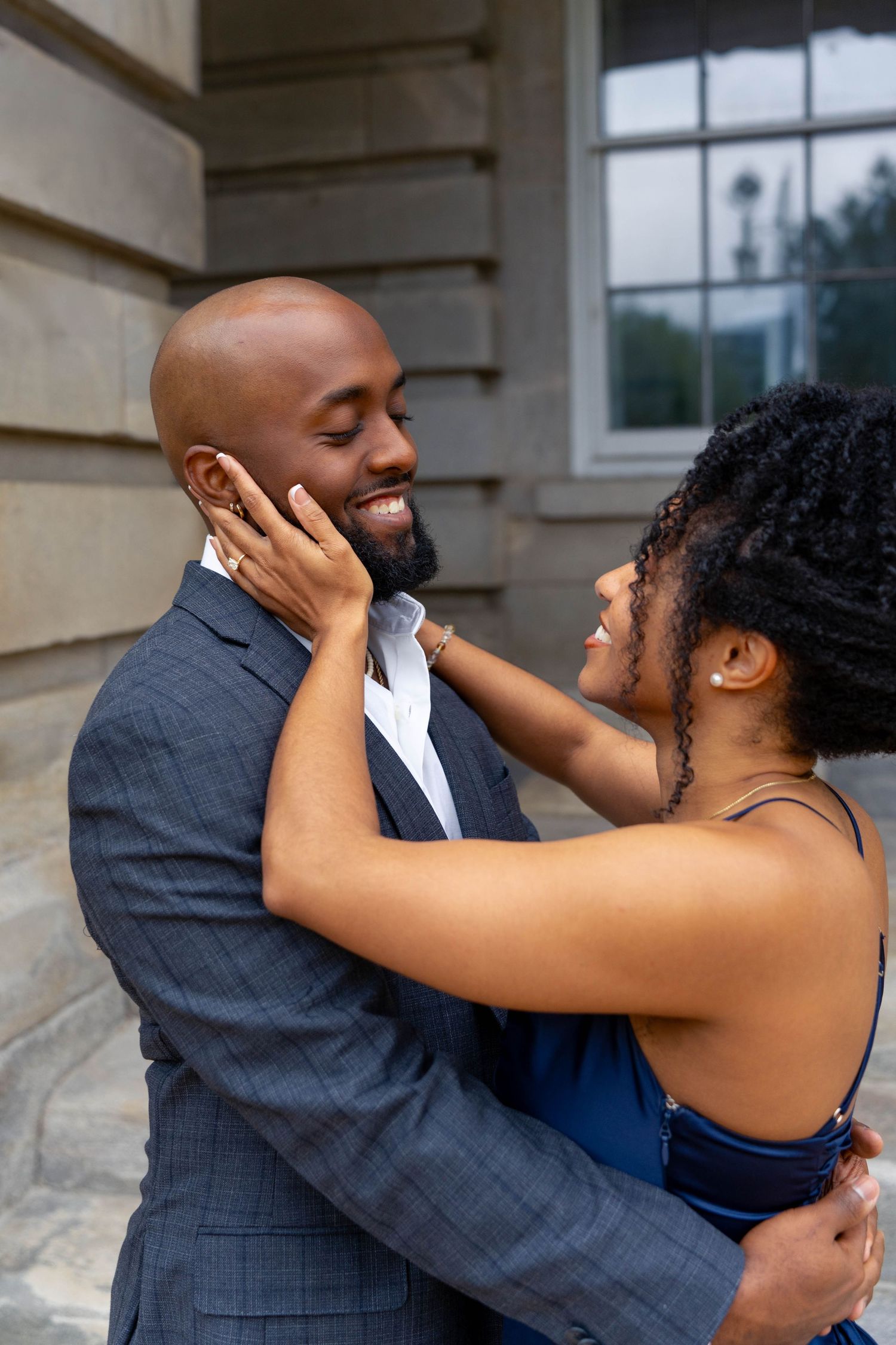 Joyful couple shares a tender moment as woman cups mans face near stone building.