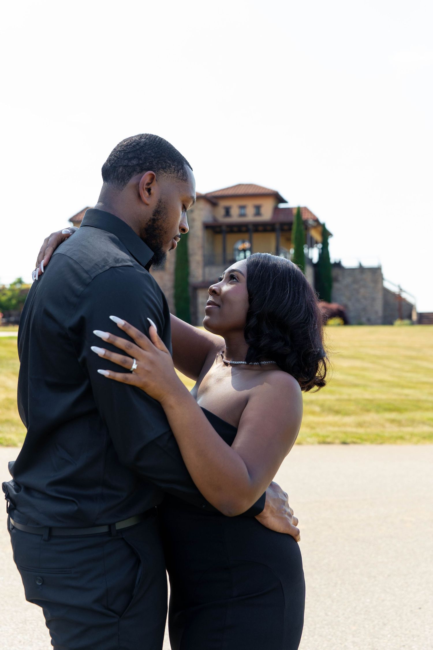 Romantic couple in black outfits gazing into each other eyes during outdoor engagement photo session.