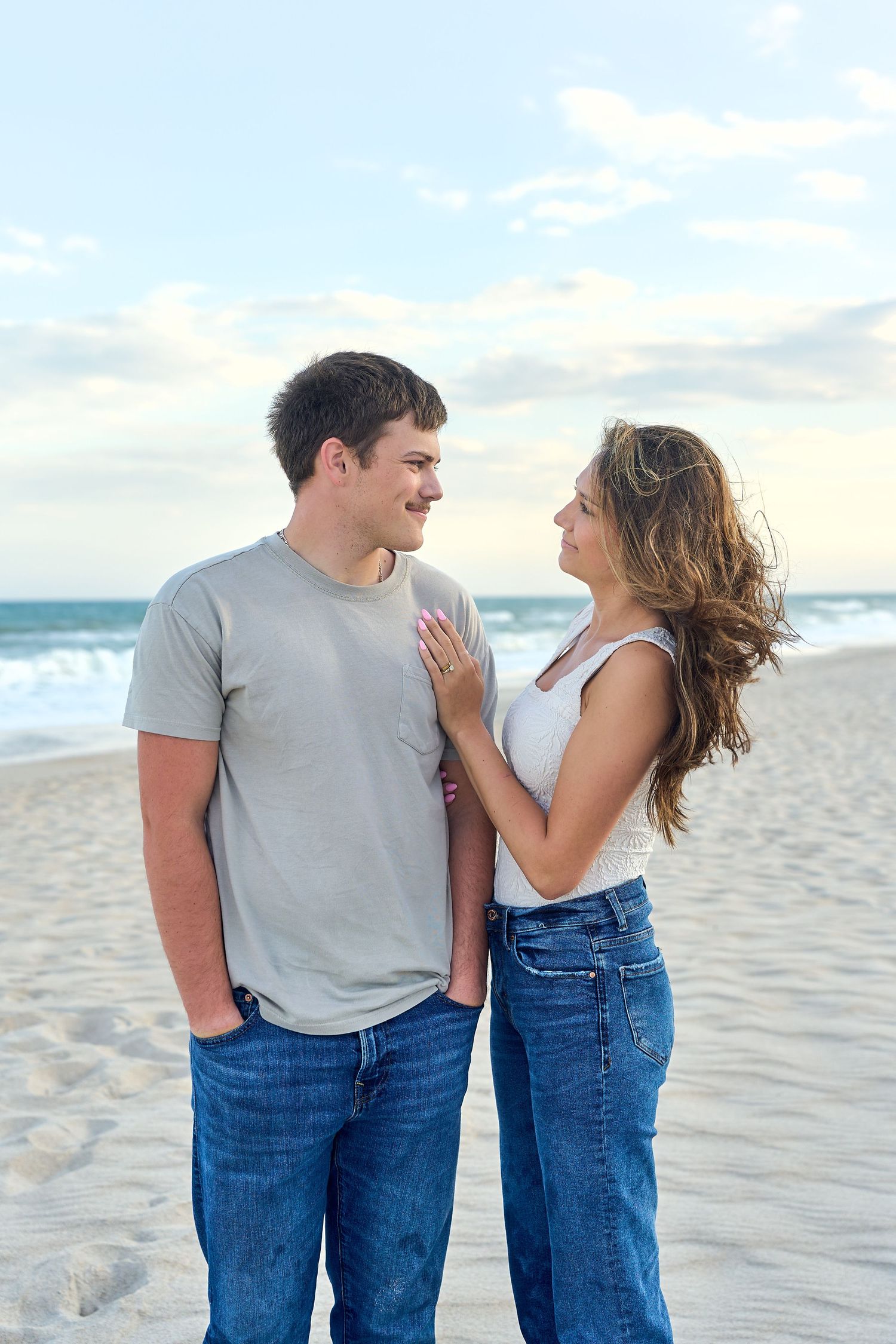 A romantic couple shares a tender moment while standing together on a sunny beach at sunset.