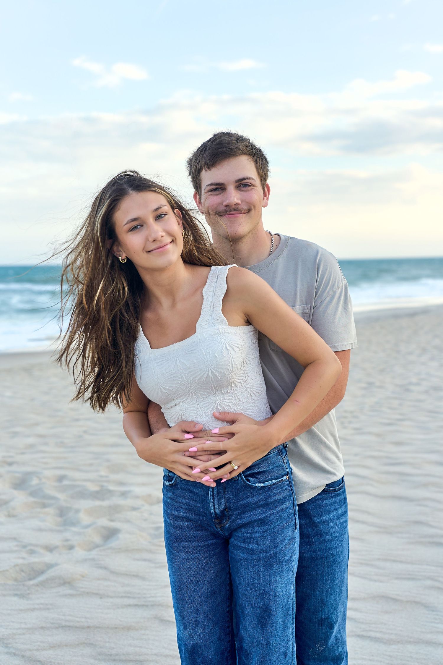 Happy couple embracing on a beach with ocean waves and blue sky in the background.