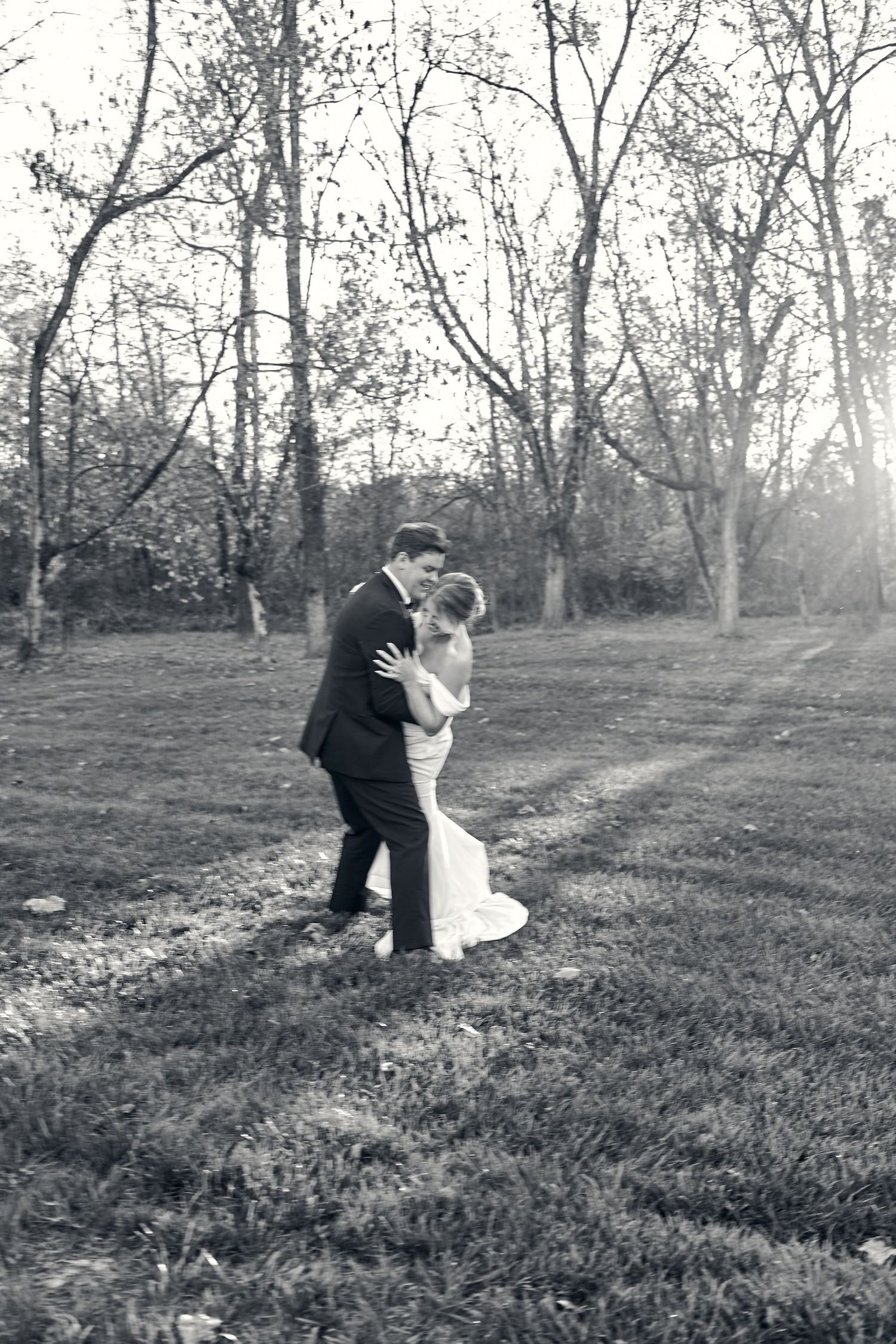 Black and white photo of bride and groom embracing romantically in a wooded field. North Carolina Wedding Photographer.