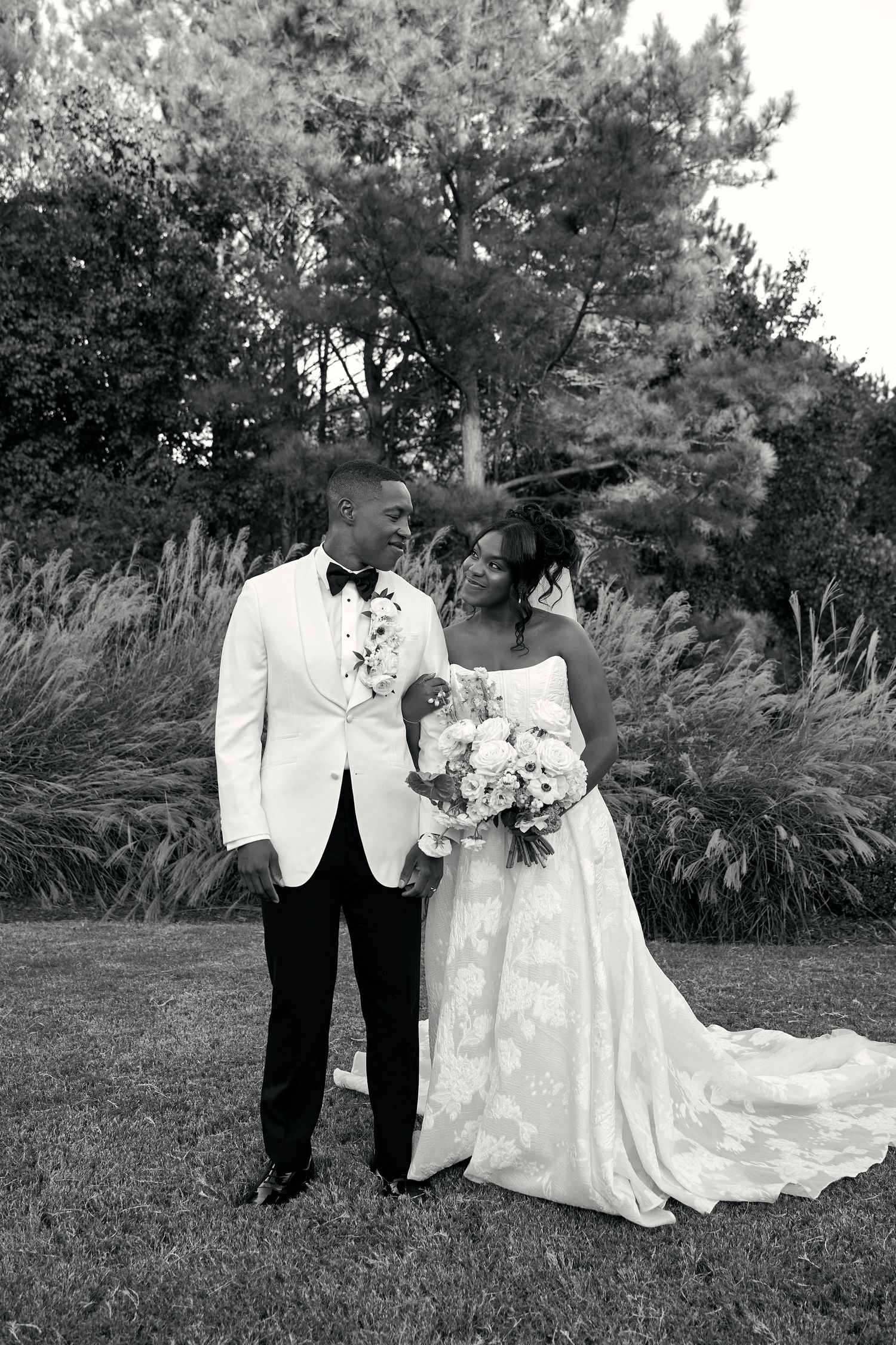 Black and white portrait of newlyweds gazing at each other in a lush garden setting.