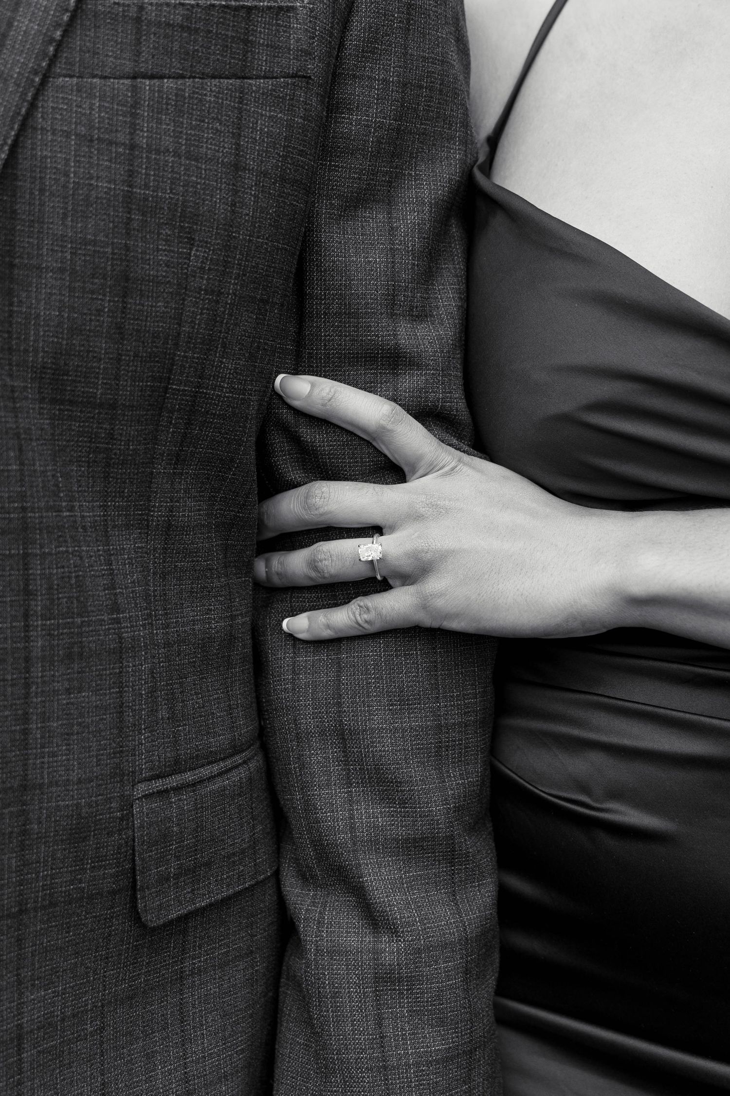 Close-up black and white photo of a woman's hand with an engagement ring gripping a man's suit jacket.