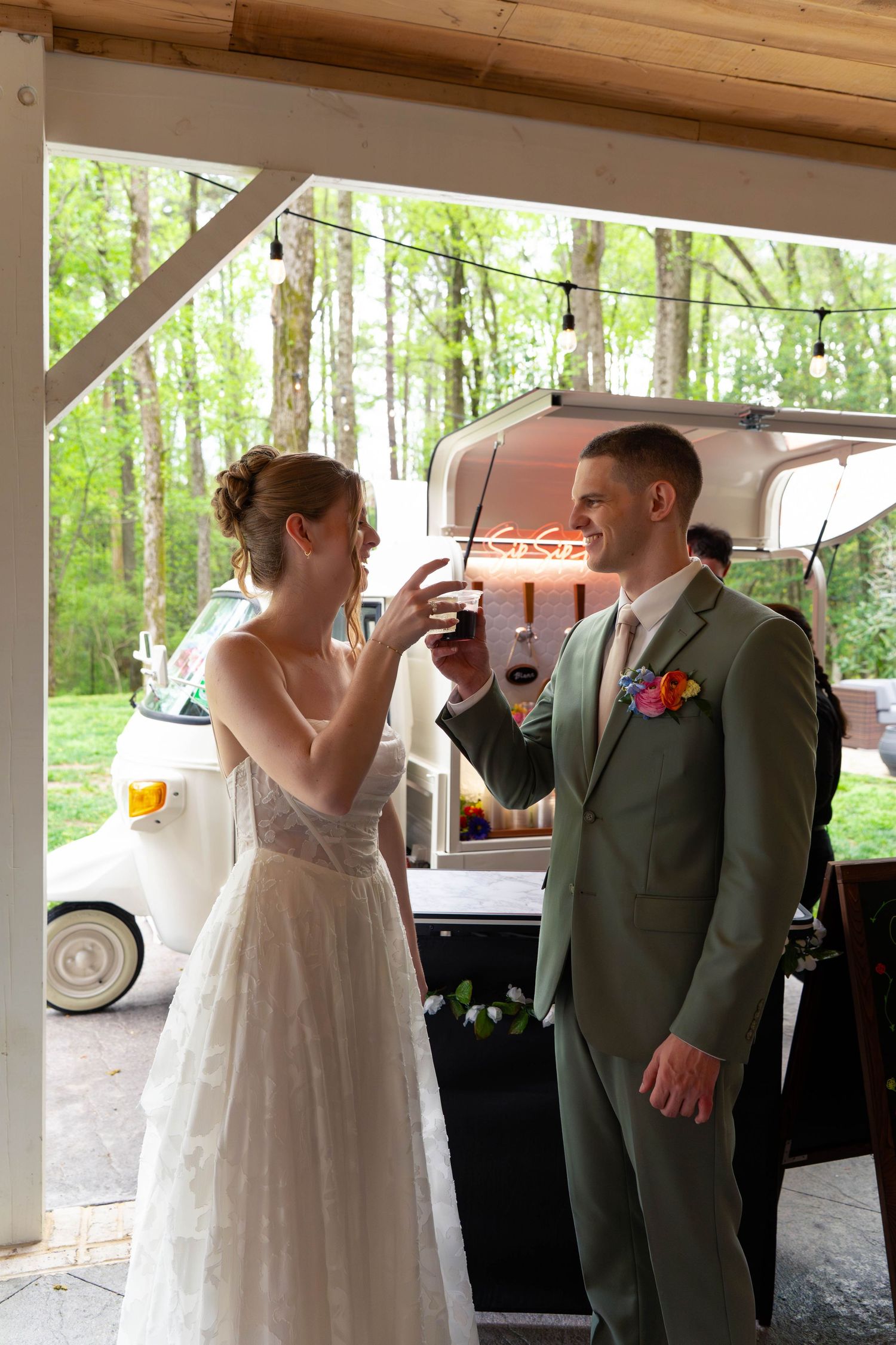 Bride and groom toasting drinks near a vintage food truck at their outdoor wedding reception.