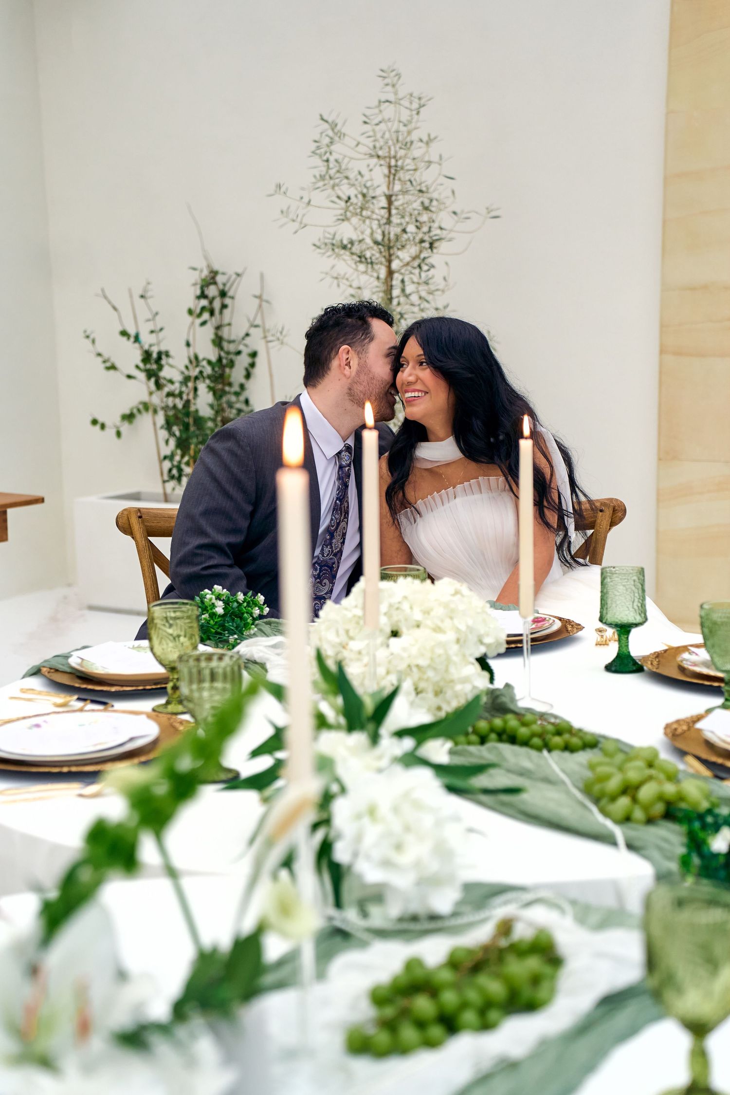 At a white tablescape with greenery and floral decor, a couple shares an intimate moment at their wedding reception.