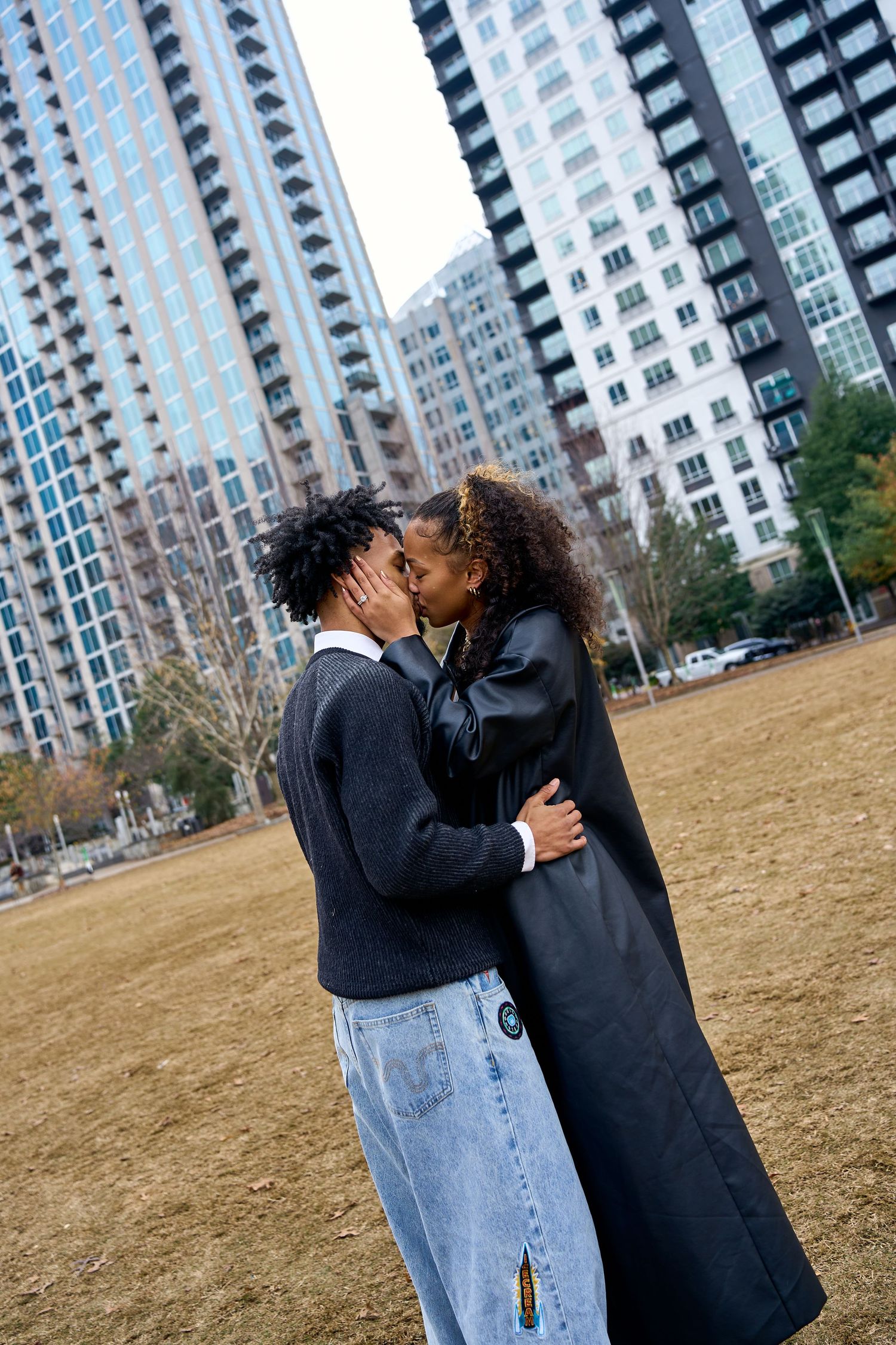 Two people share an intimate moment together while standing on a field with high-rise buildings in background. North Carolina Photographer.