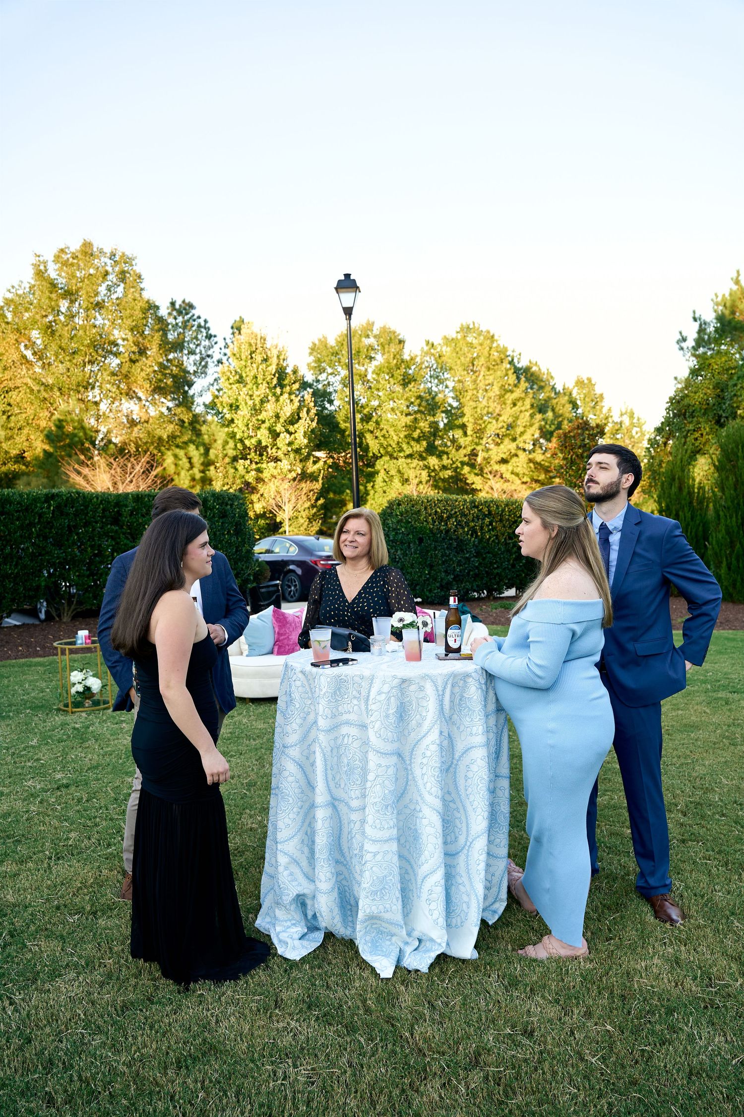 Elegantly dressed wedding guests mingle around a cocktail table outdoors during a garden reception.