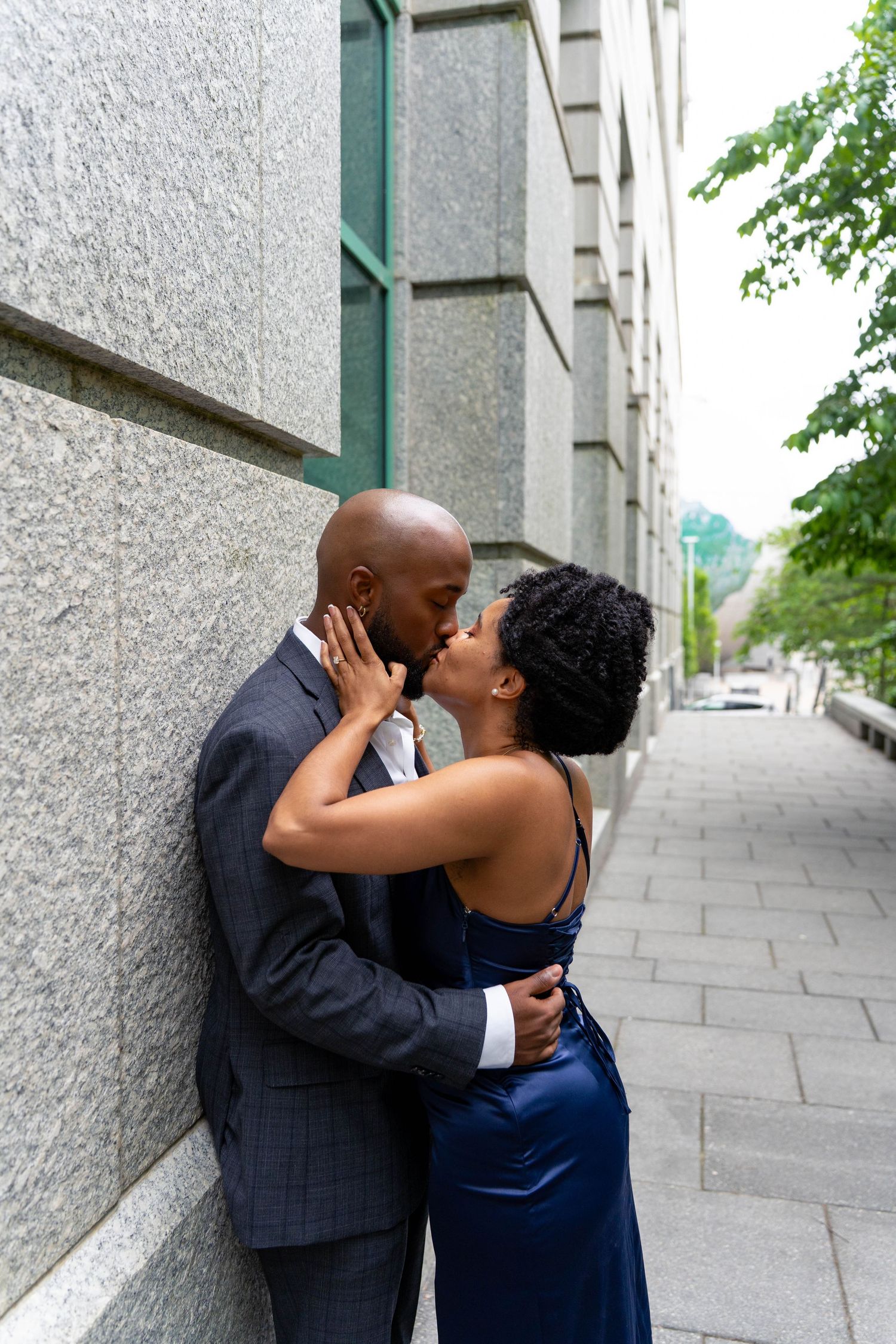 Black couple sharing a passionate kiss against a granite stone wall on a city sidewalk.