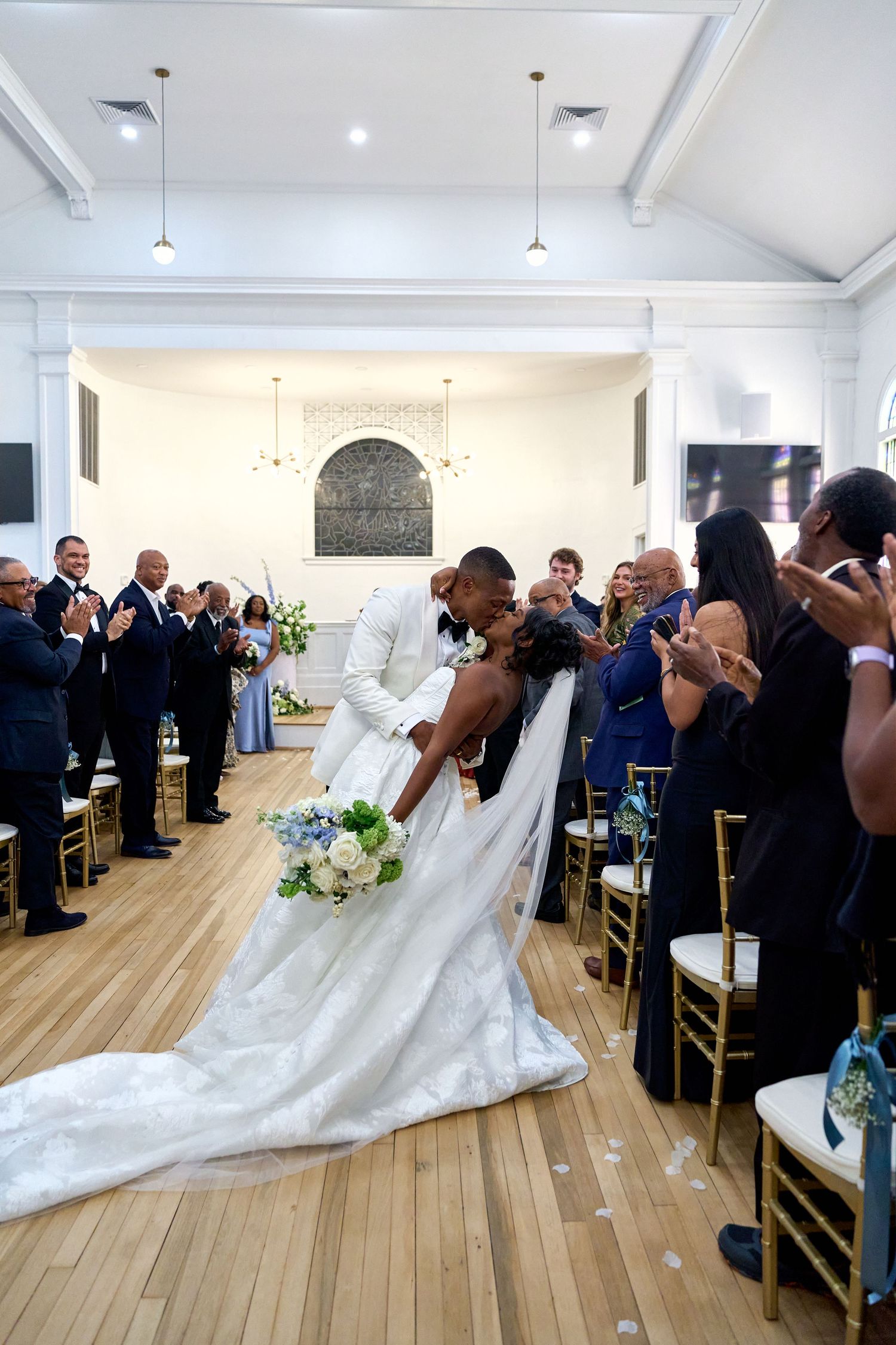 Groom dips bride for romantic kiss in church aisle as wedding guests applaud the newlyweds.