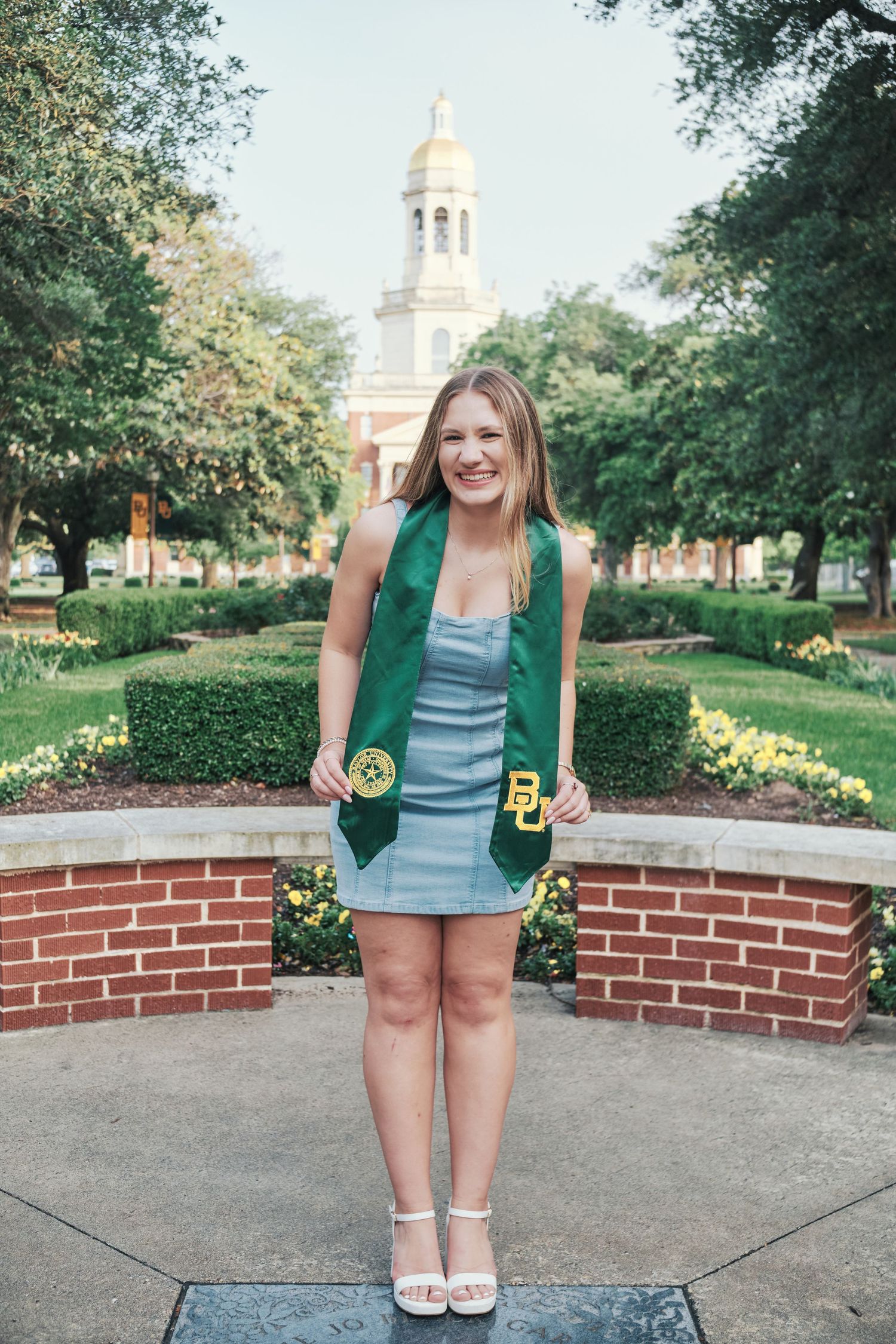 Smiling Baylor University graduate poses with green BU stole in front of historic campus building. North Carolina Photographer.