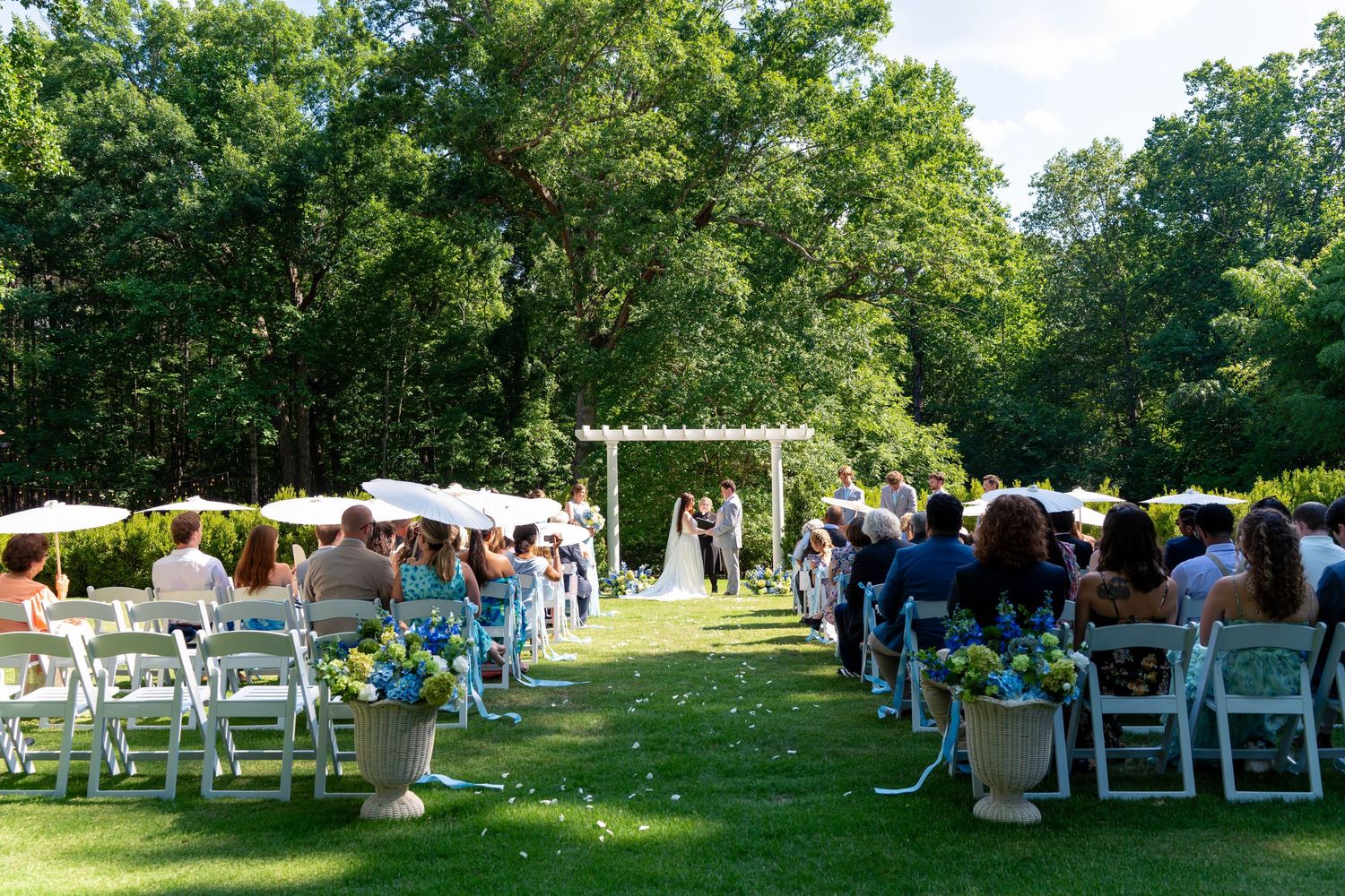 Outdoor wedding ceremony on lush lawn with white chairs and floral arrangements.