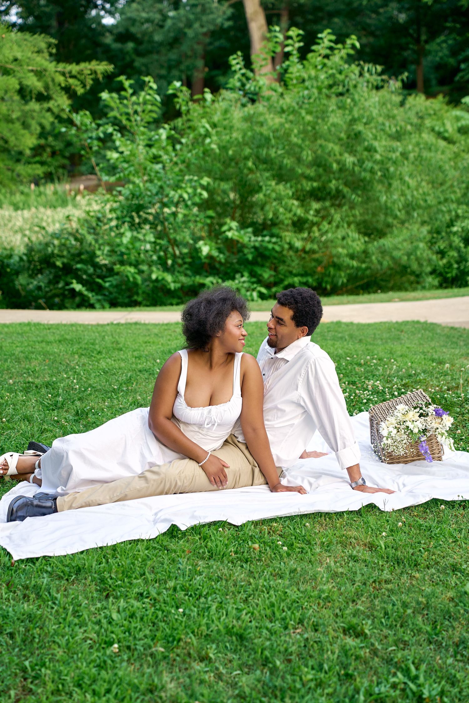 A couple relaxes on a white blanket having a romantic picnic on green grass.