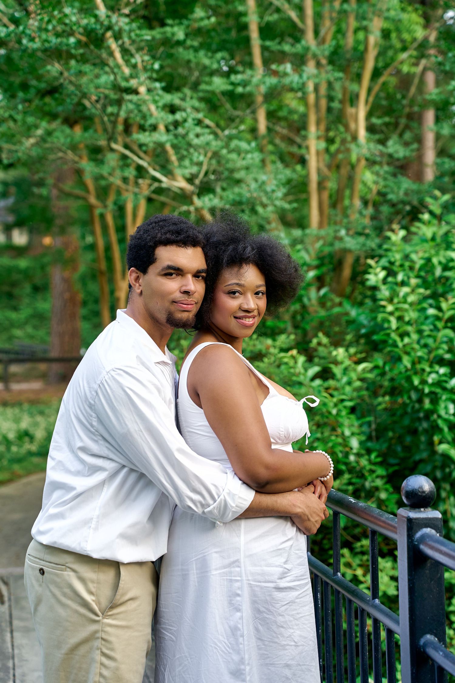 A couple embracing on a garden pathway surrounded by green foliage and trees.