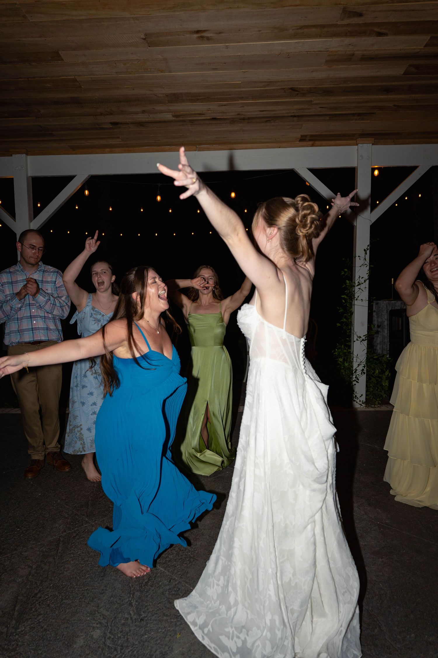 Bride dancing with guests in colorful gowns at a lively outdoor wedding reception at night.