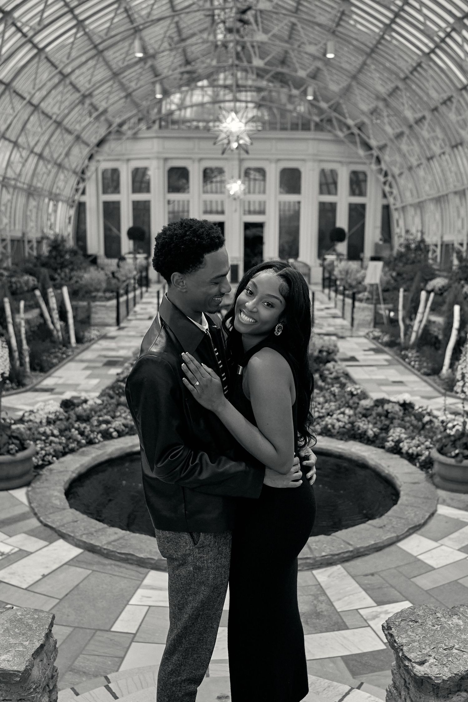 Black and white romantic portrait of a couple embracing inside an elegant domed botanical conservatory.