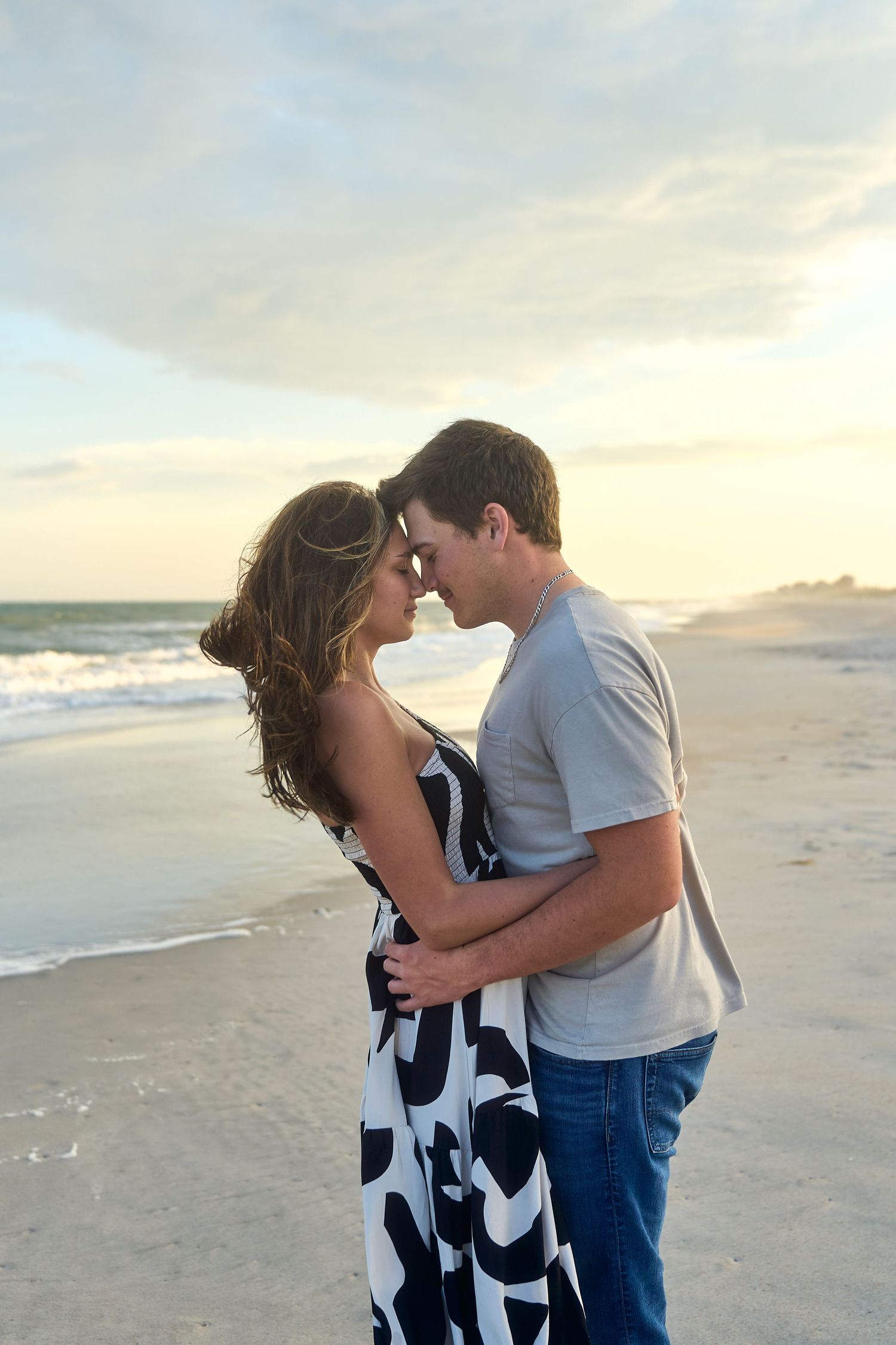 A romantic couple shares an intimate moment at sunset on a serene beach with waves rolling in the background.