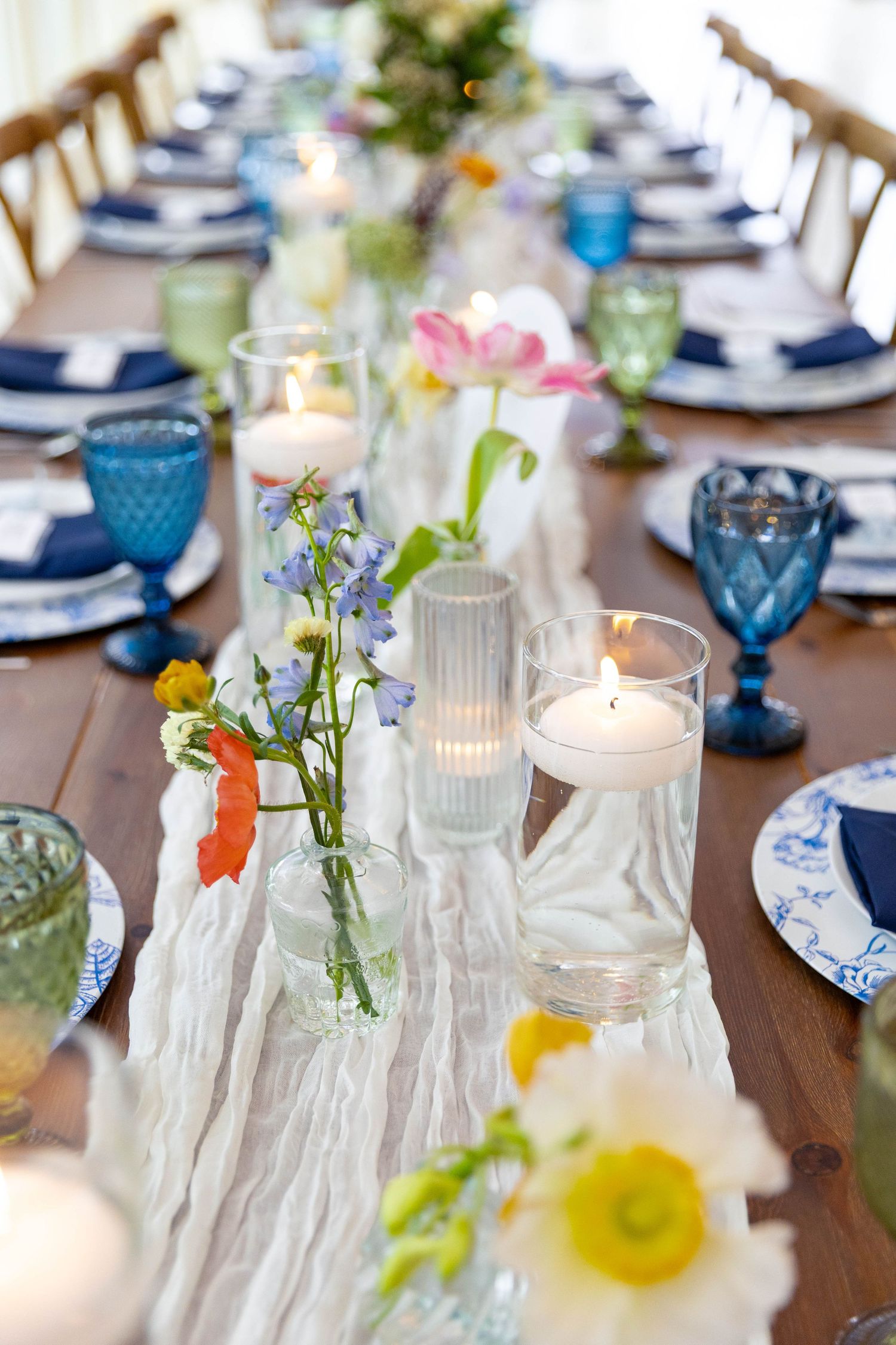 Elegant wedding reception table with blue glassware, colorful wildflowers, and floating candles.