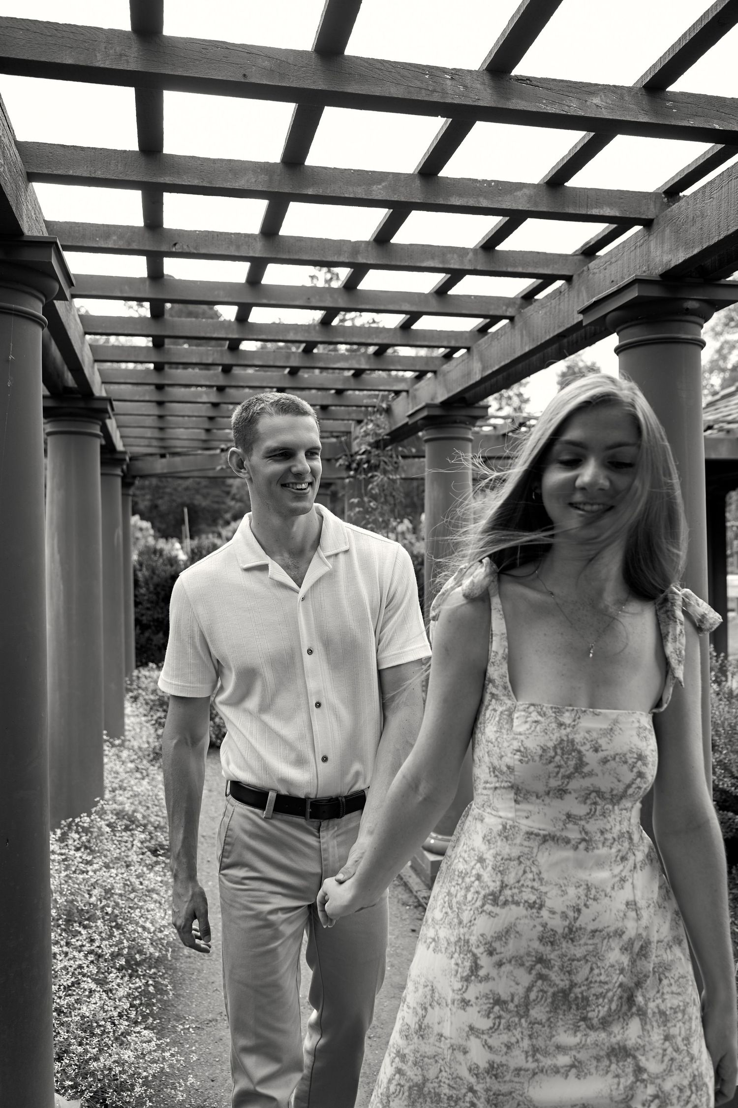 Black and white photo of a couple sharing a joyful moment under a pergola structure. North Carolina Wedding Photographer.