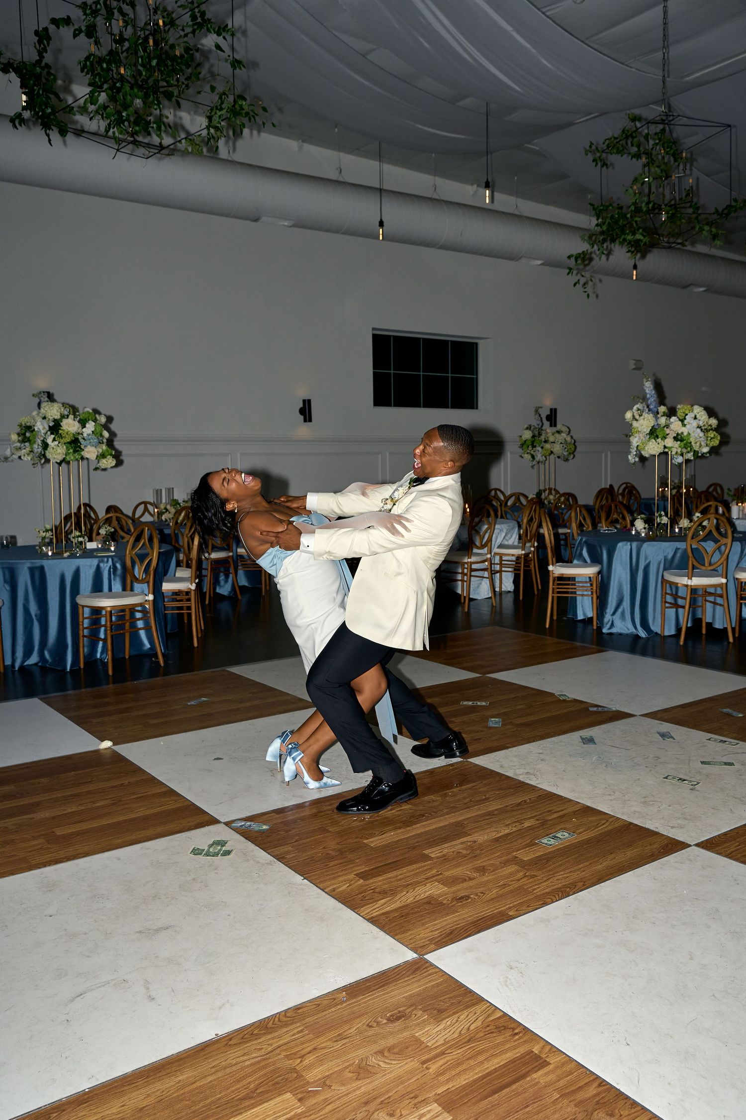 Couple performs a dramatic dip on a checkered dance floor at a beautifully decorated wedding reception.