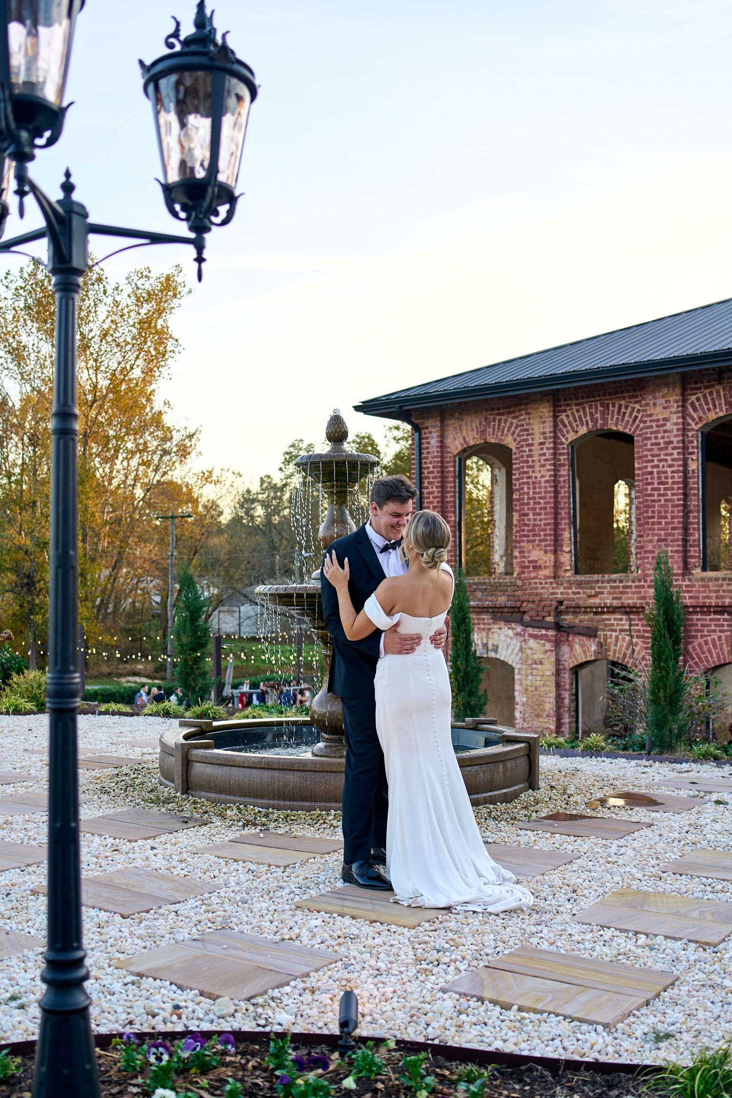 Bride and groom share romantic dance near stone fountain outside elegant brick venue. North Carolina Wedding Photographer.
