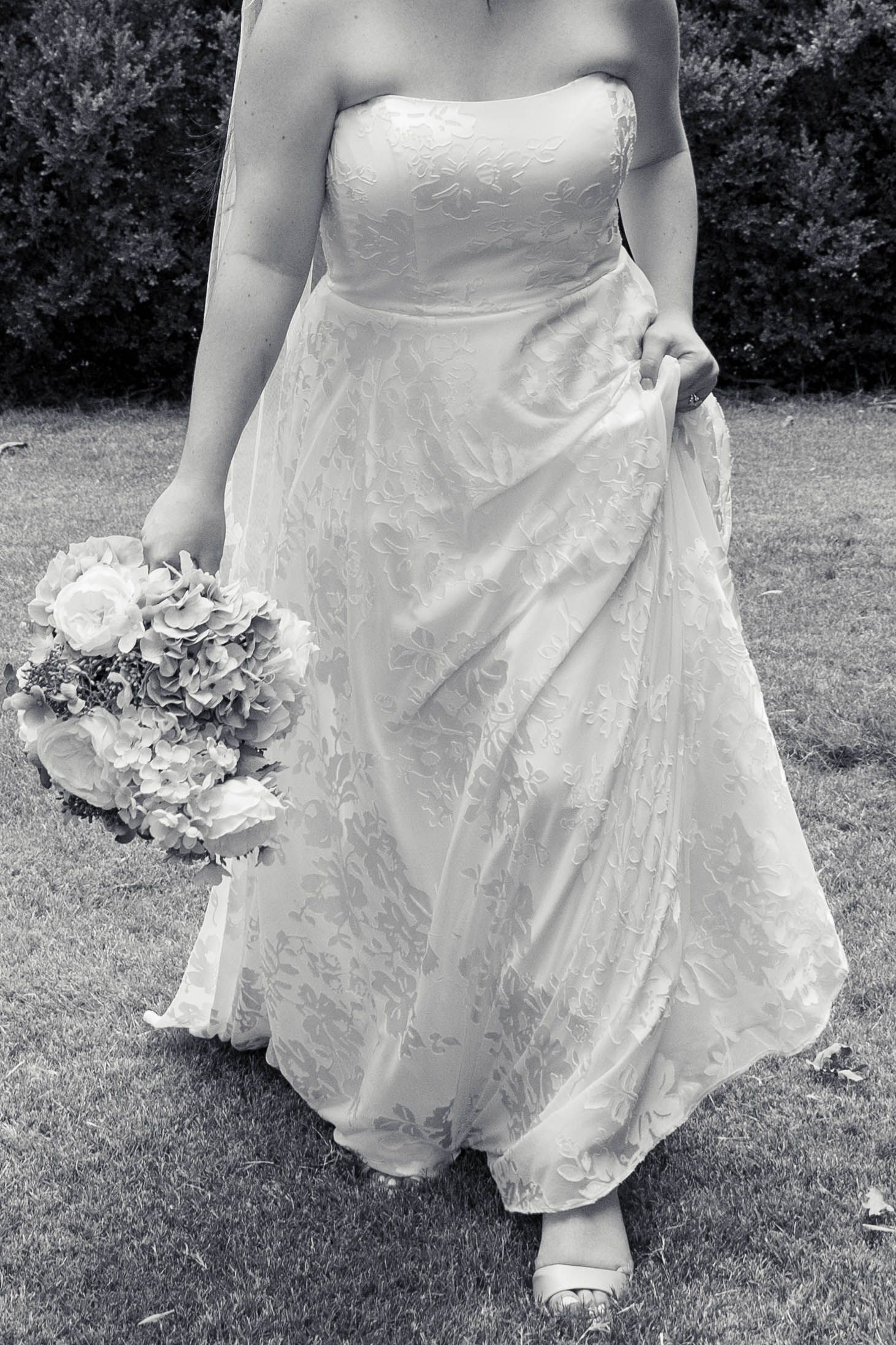Bride in strapless white lace gown stands at black door holding blue and white hydrangea bouquet.