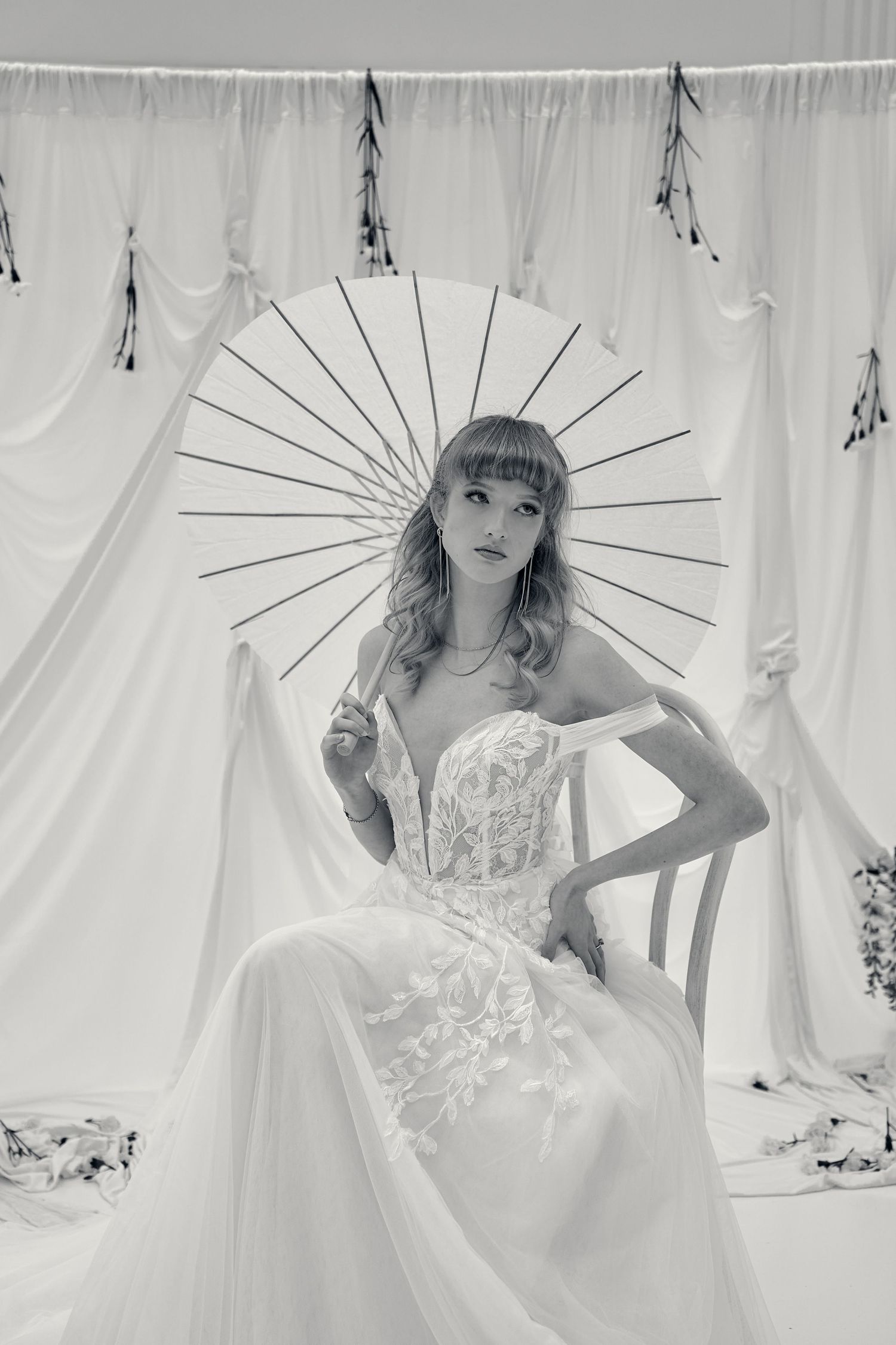 Black and white photograph of a bride in a strapless lace wedding gown posing with a paper parasol against a white backdrop.