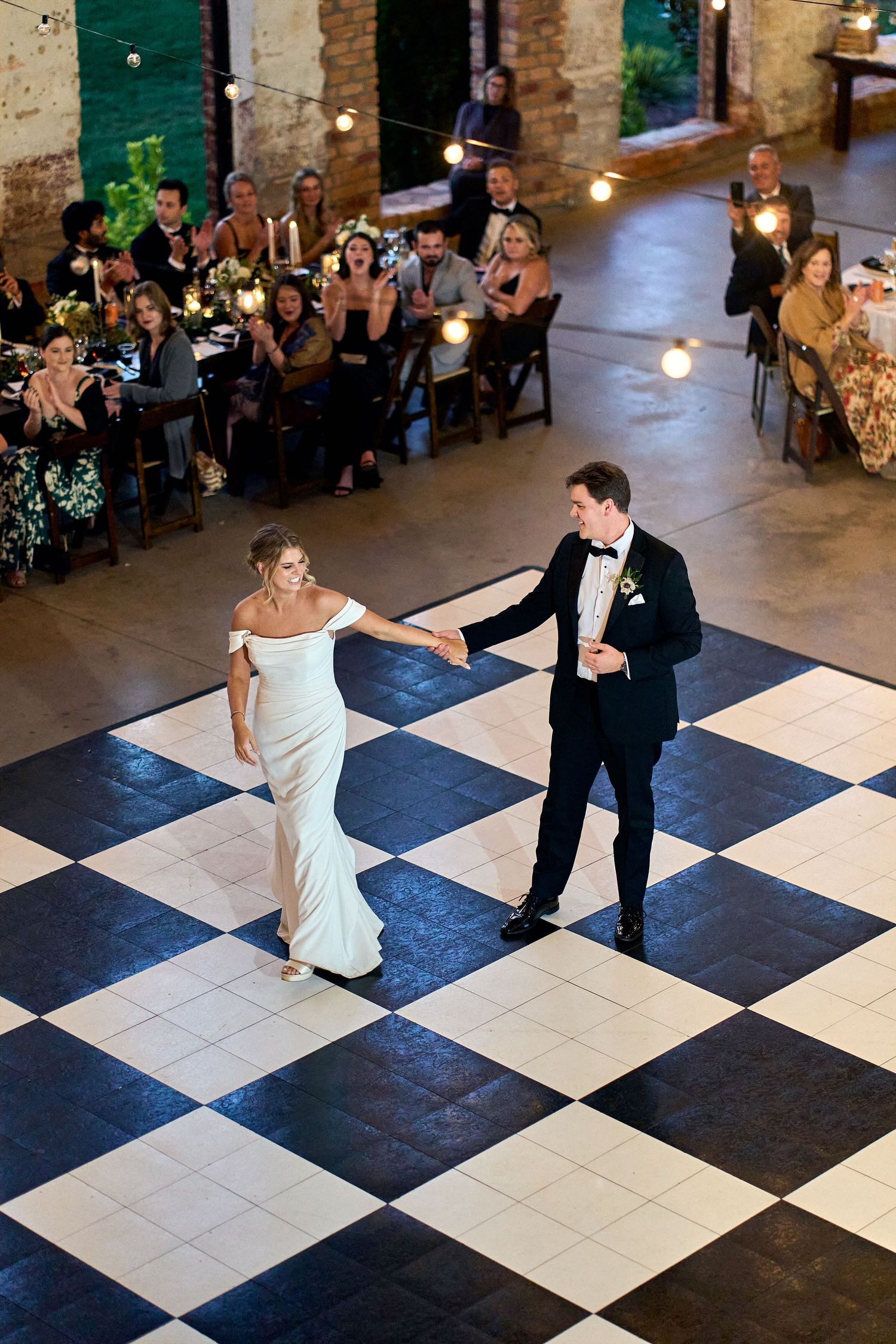Bird's eye view of a couple dancing on a black and white checkered floor at an elegant indoor reception venue.