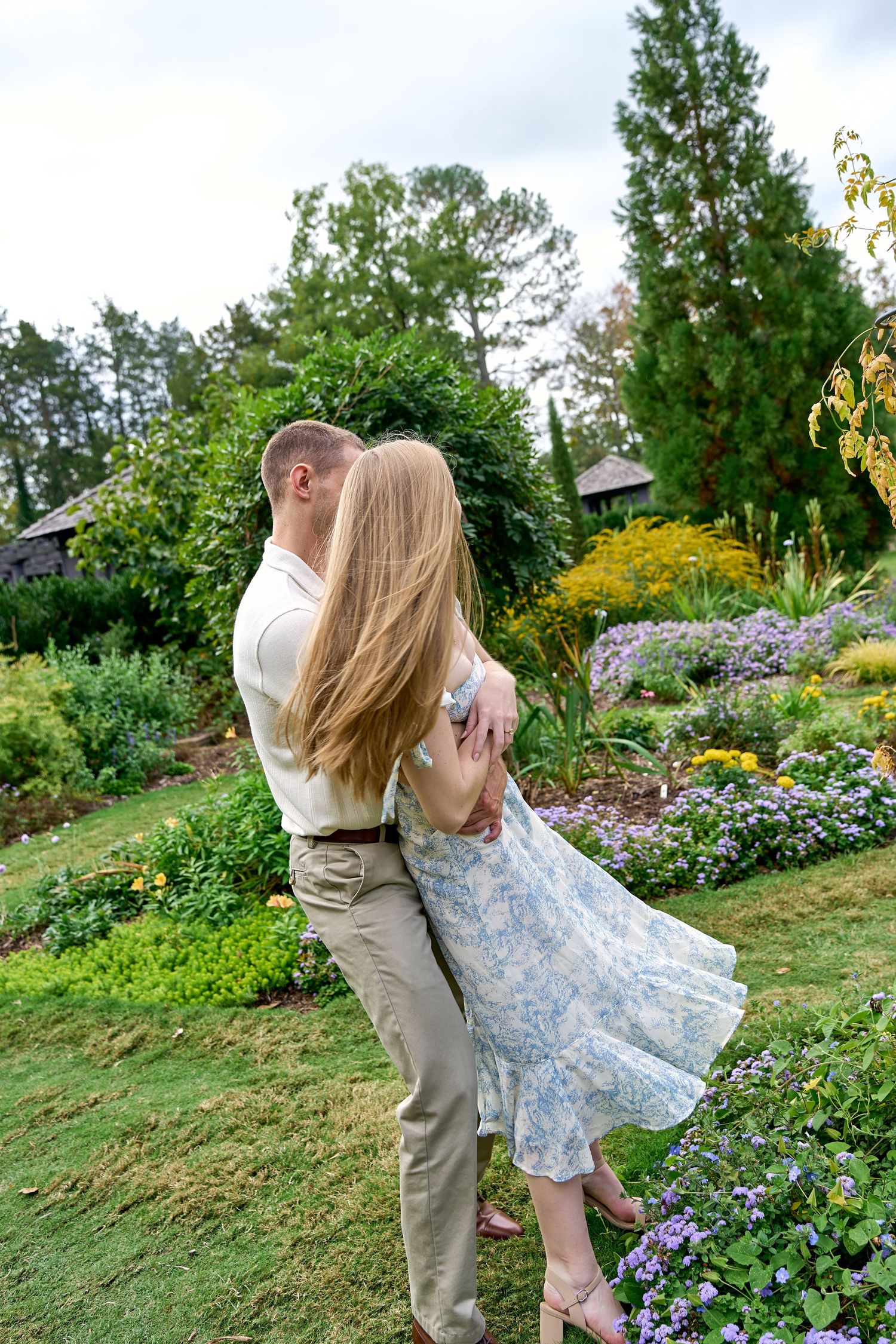 A couple dances playfully in a lush garden with blooming flowers and greenery. North Carolina Wedding Photographer.