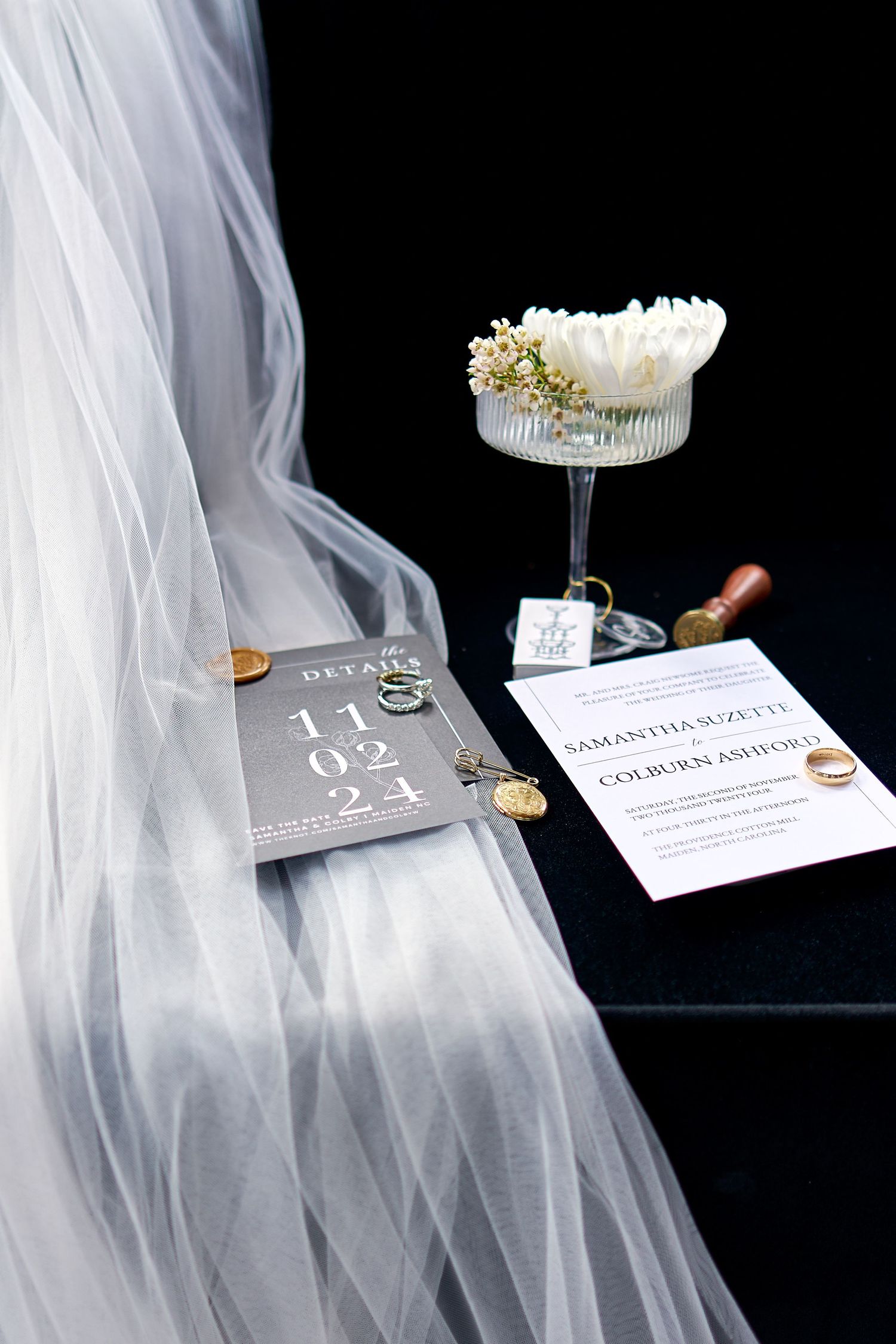 Wedding flat lay featuring veil, invitation suite, rings, and floral coupe glass display. North Carolina Wedding Photographer.