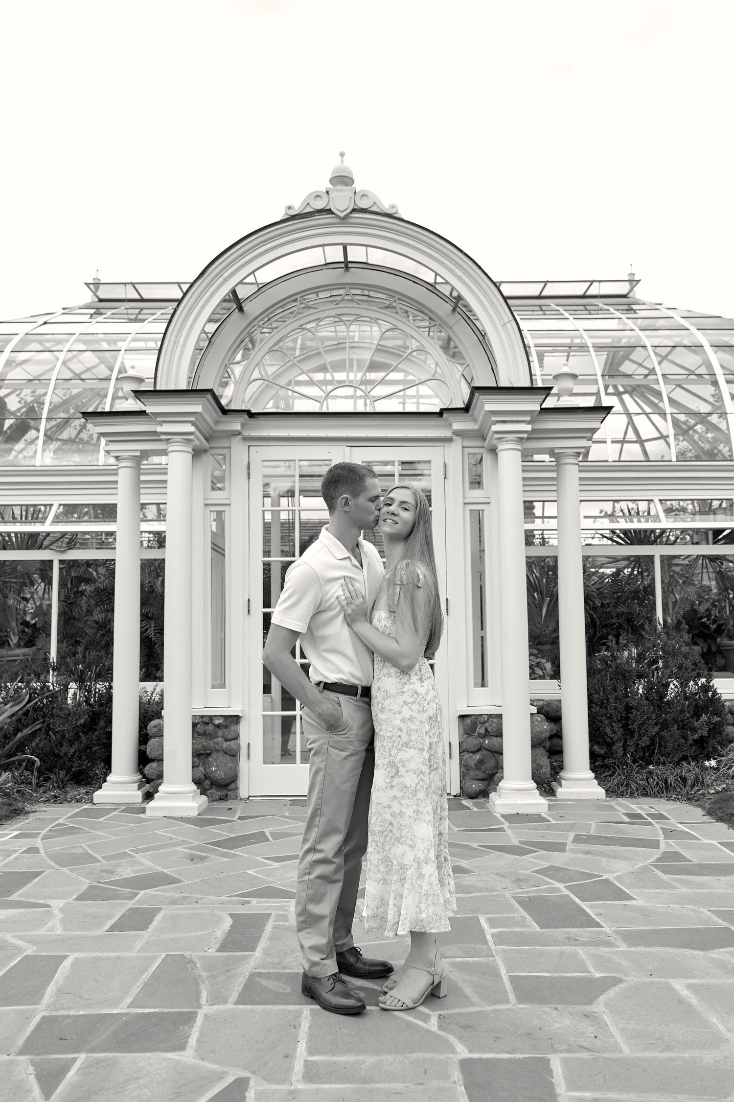 A couple embraces under an elegant white conservatory archway with stone flooring. North Carolina Wedding Photographer.