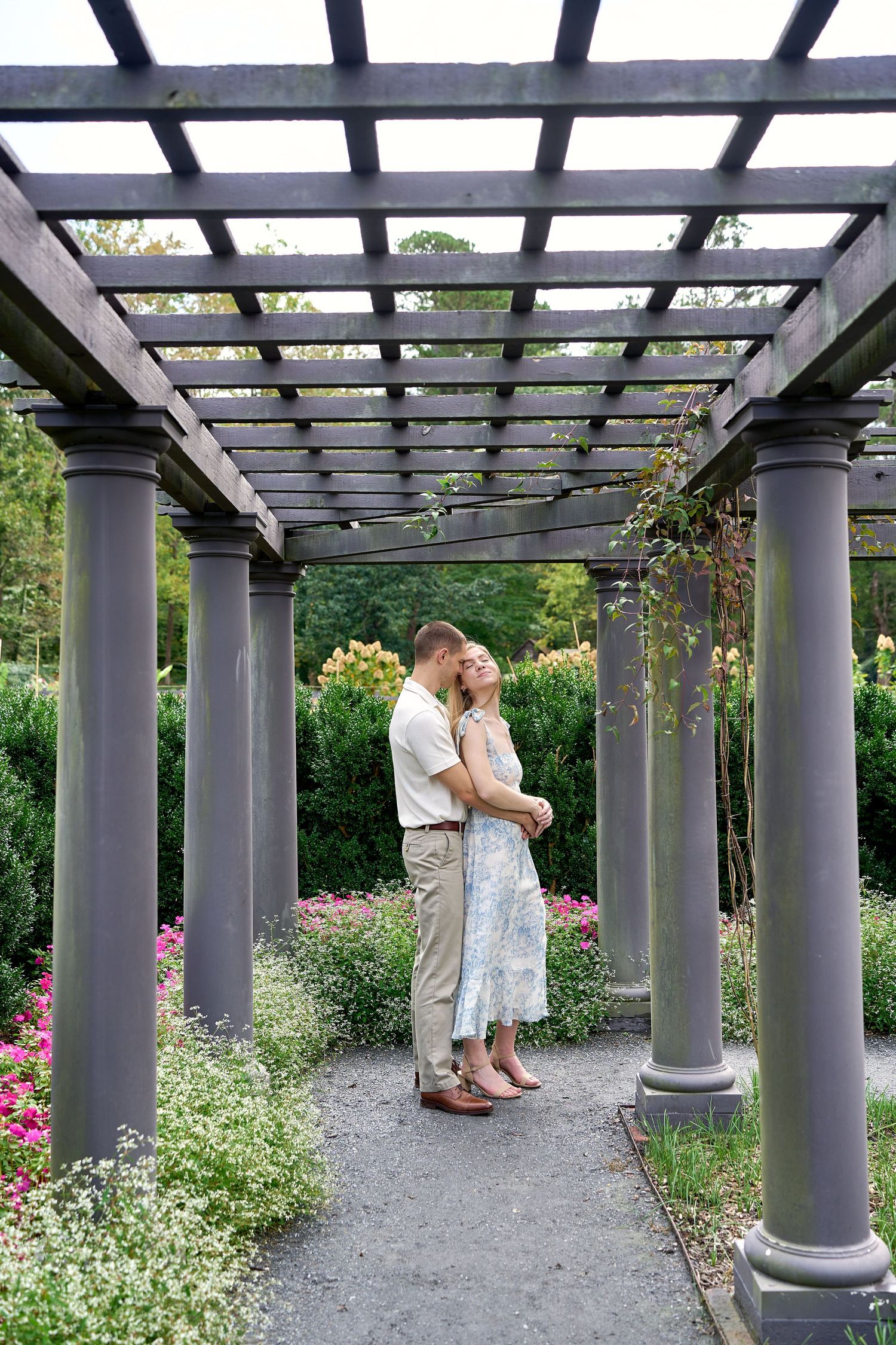A romantic scene under a pergola with gray columns in a garden setting. North Carolina Wedding Photographer.