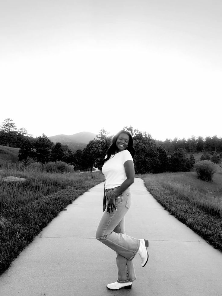 Young woman smiling on a pathway surrounded by scenic mountains and trees in a black and white photo.