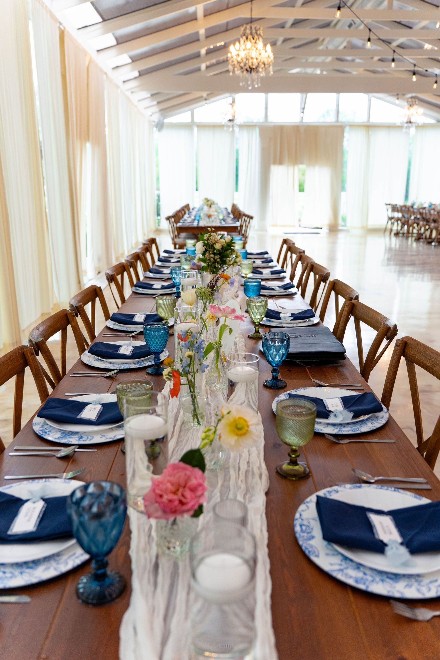 Long wooden wedding reception table set with blue napkins, floral centerpieces, and blue goblets.