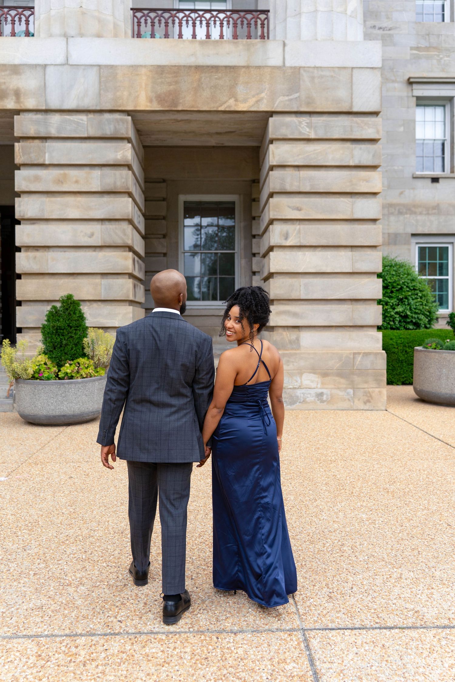 Stylish Black couple holding hands walking toward a grand stone building, woman in blue satin gown.