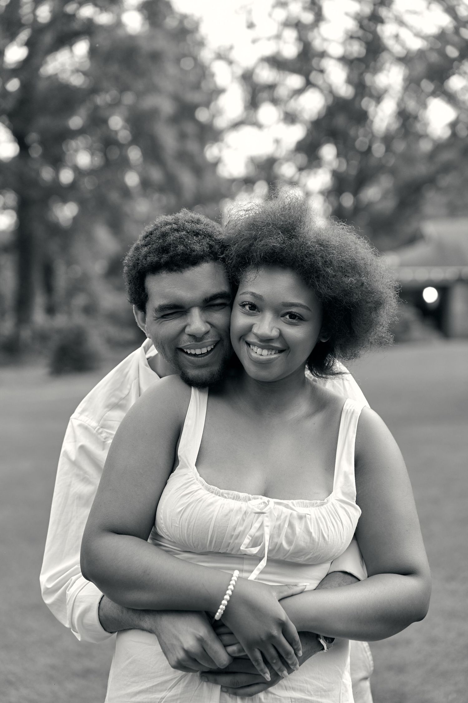 Four heartwarming black and white photos show a sweet embrace between two people wearing white outfits outdoors.
