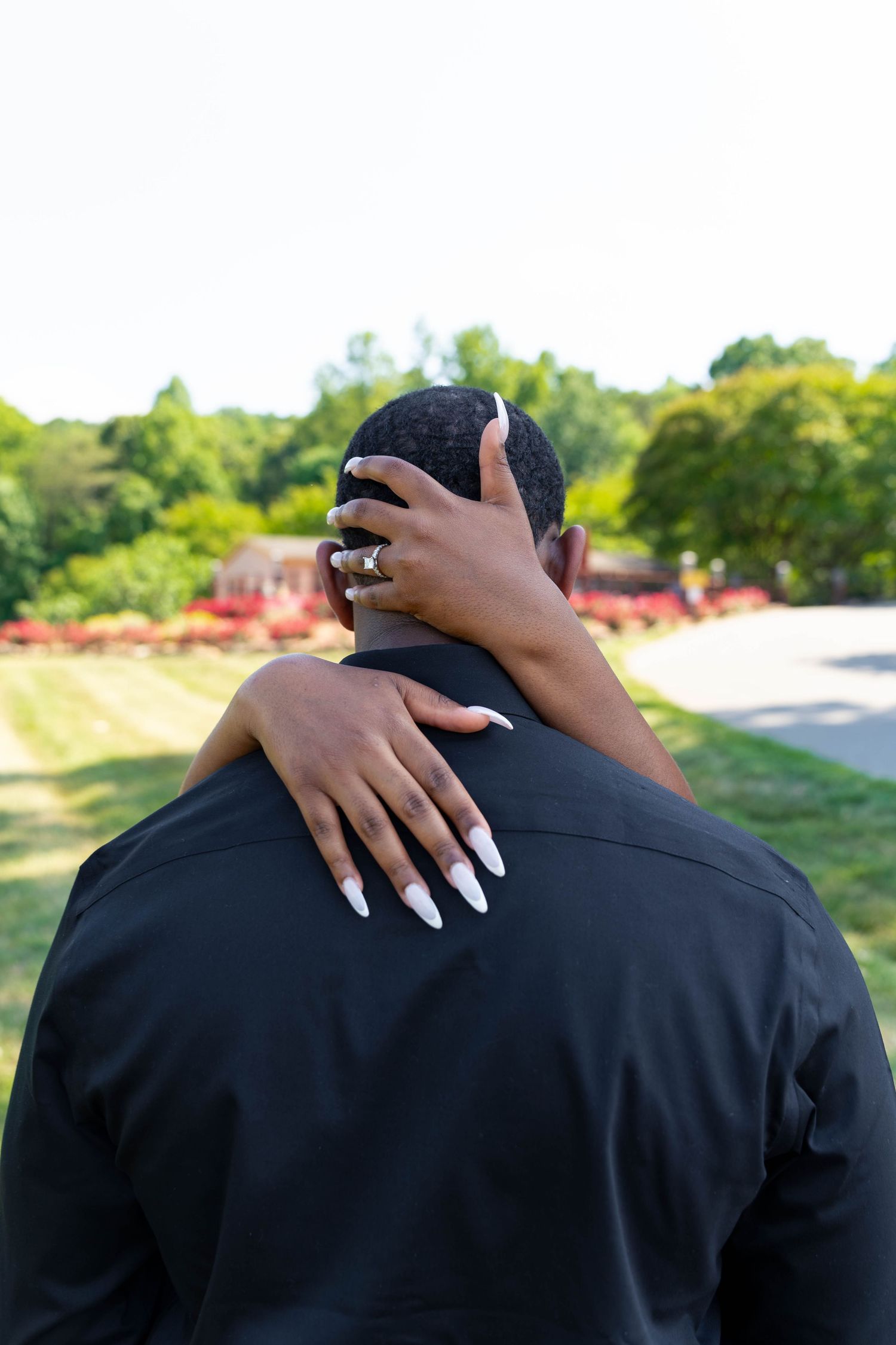 Close-up of a woman placing her hand with engagement ring on a mans neck outdoors.