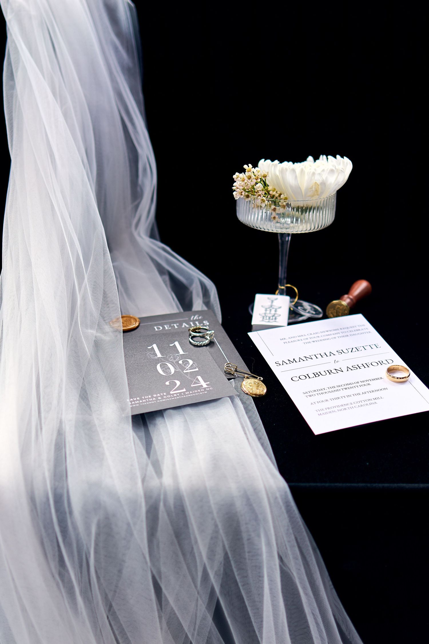 Wedding veil draped elegantly beside a cocktail glass and invitation cards on a dark surface.