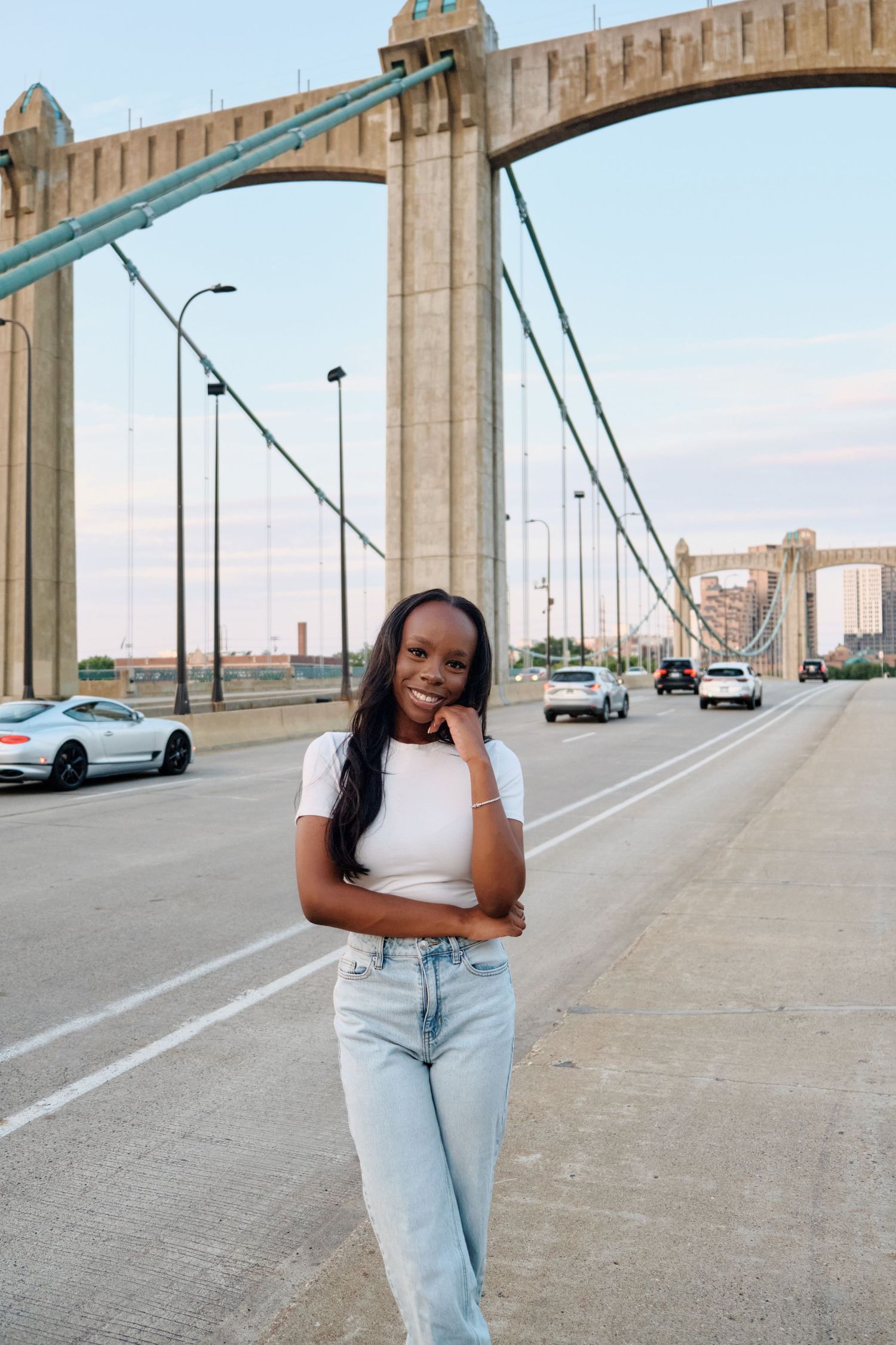 Young woman in white tee and jeans poses confidently on a busy bridge at dusk. North Carolina Photographer.