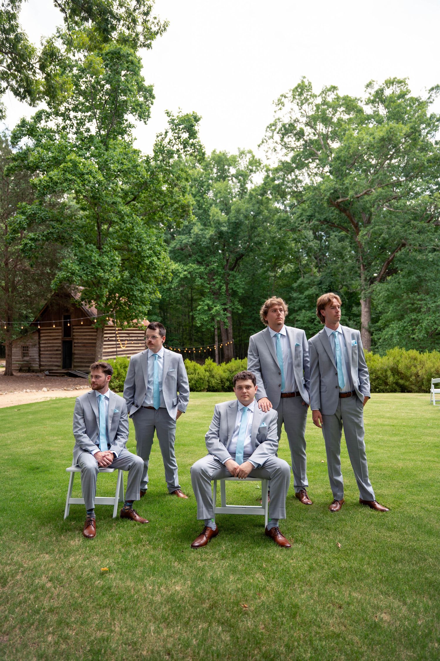 Groom and four groomsmen in matching gray suits with blue ties pose on green lawn.