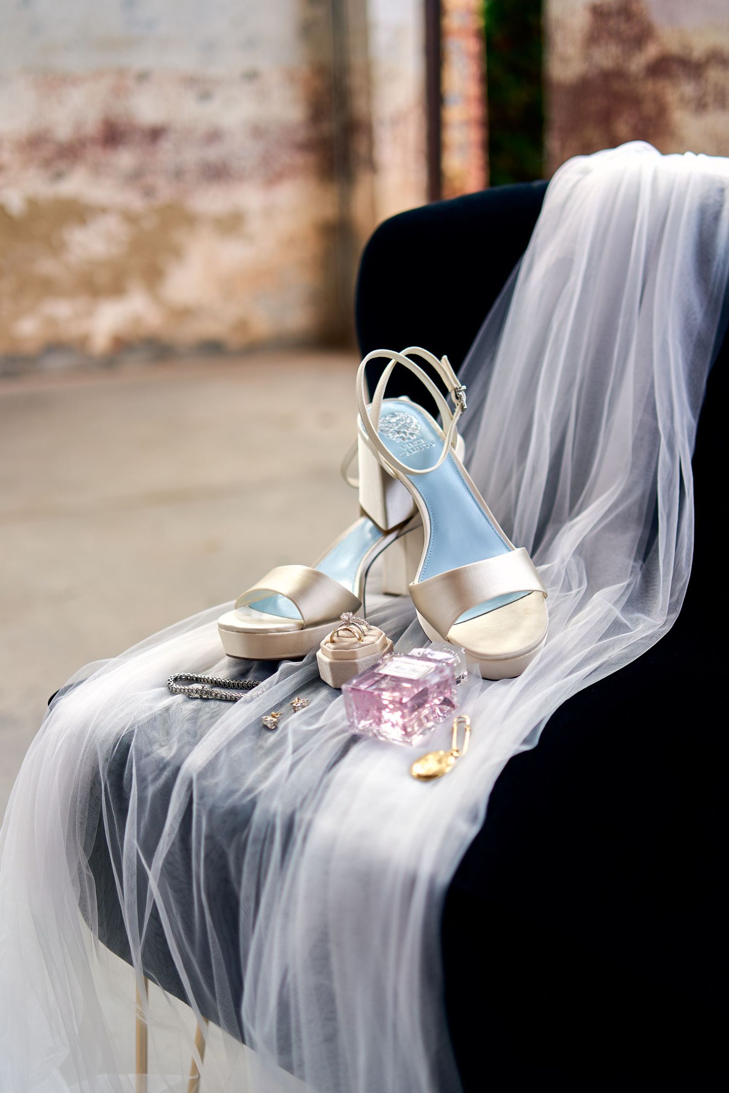 Elegant bridal high heel shoes in light blue displayed with wedding veil and perfume bottle on black surface.