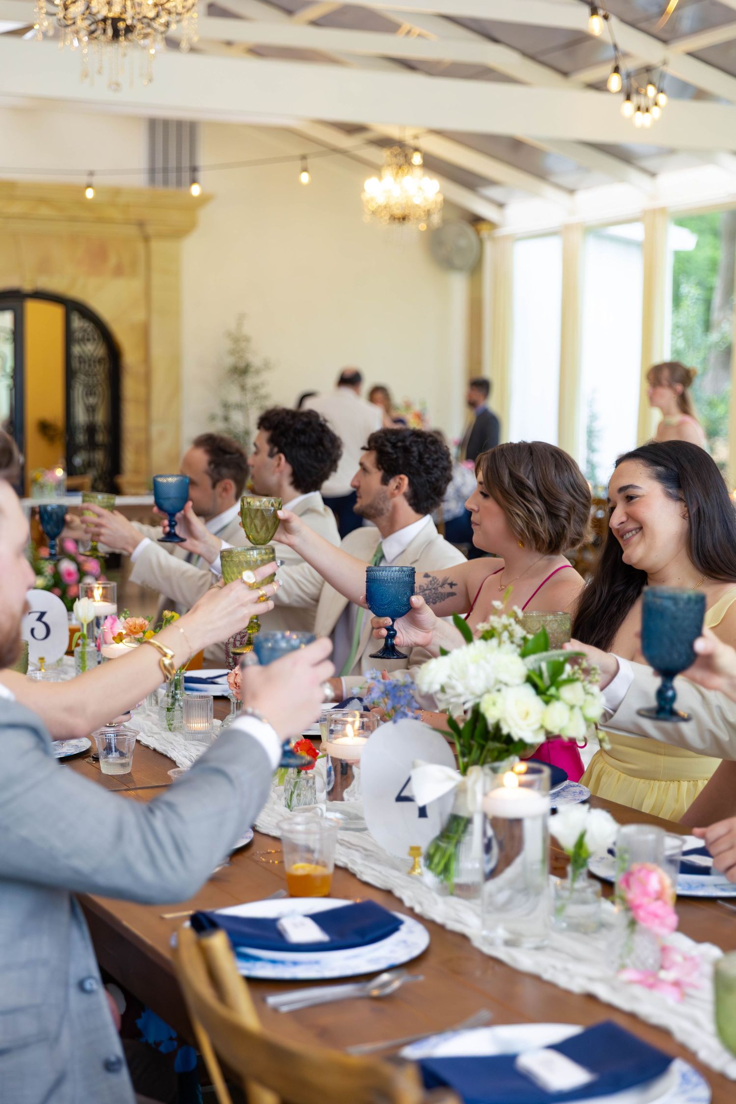 Wedding guests raising blue goblets in a toast at an elegant indoor reception dinner.