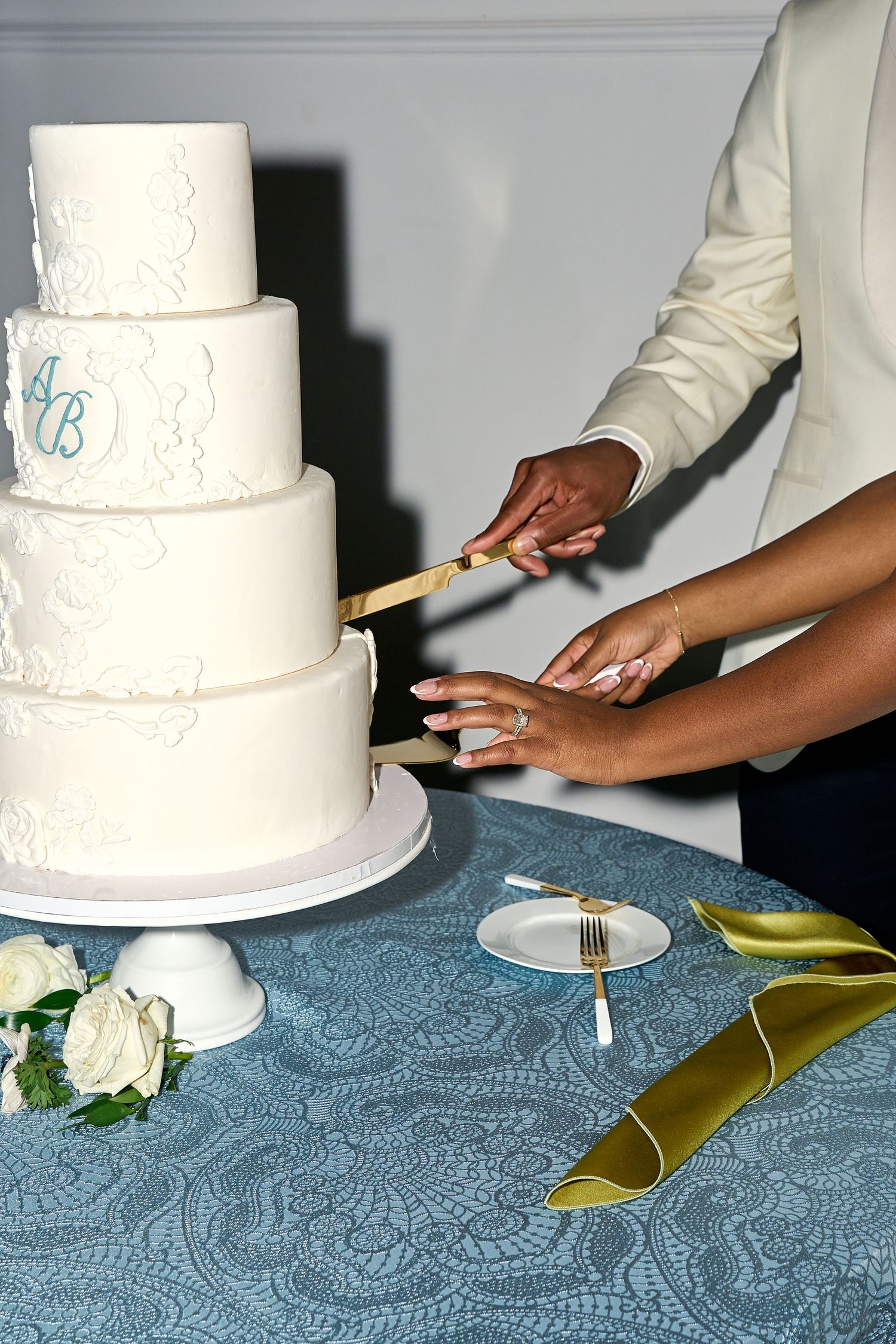 Bride and groom cut four-tier white wedding cake with gold knife at elegant wedding reception.