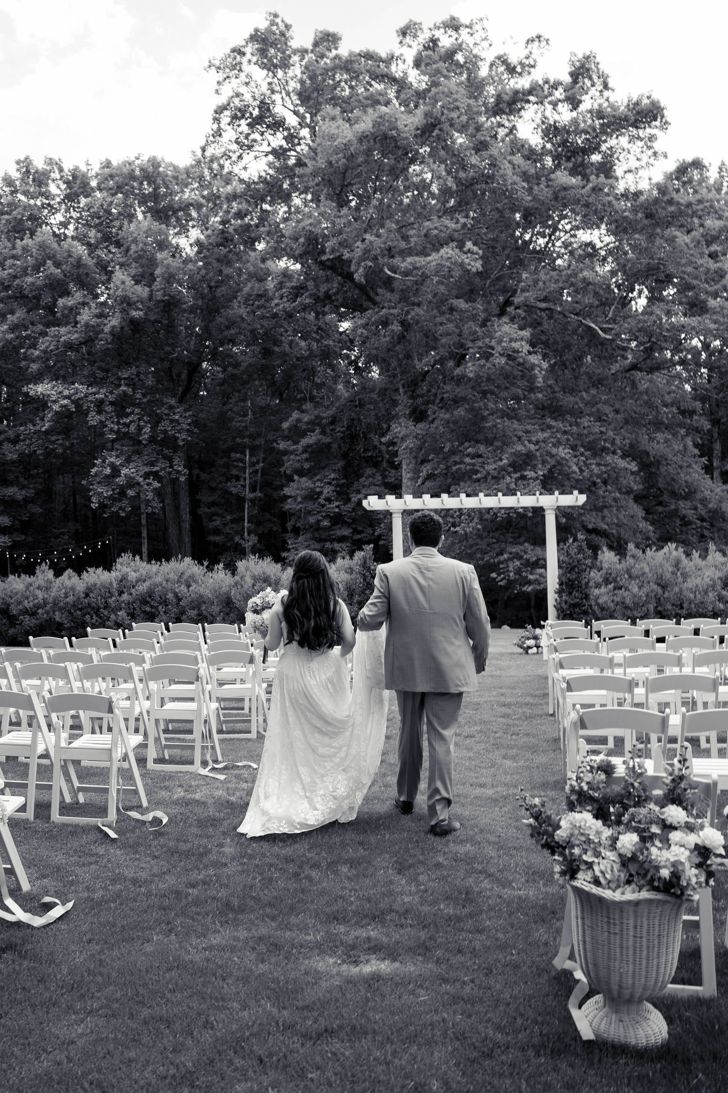 Black and white photo of bride and groom walking down outdoor ceremony aisle.