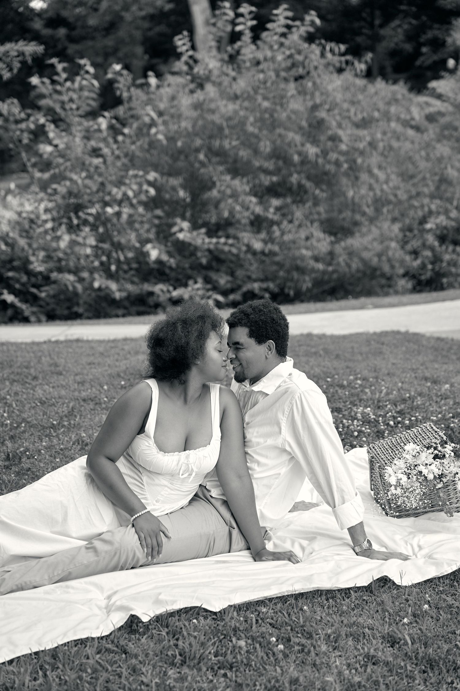 A romantic couple in white clothing relaxes together on a blanket in a grassy outdoor setting.