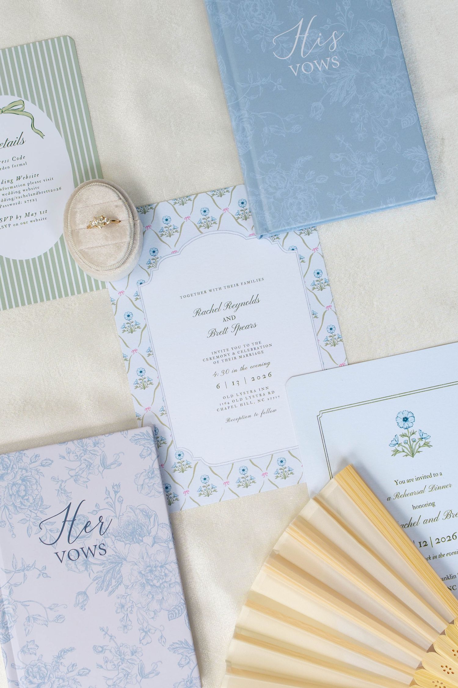 Wedding stationery flat lay with vow books, invitation, and fans in blue tones.