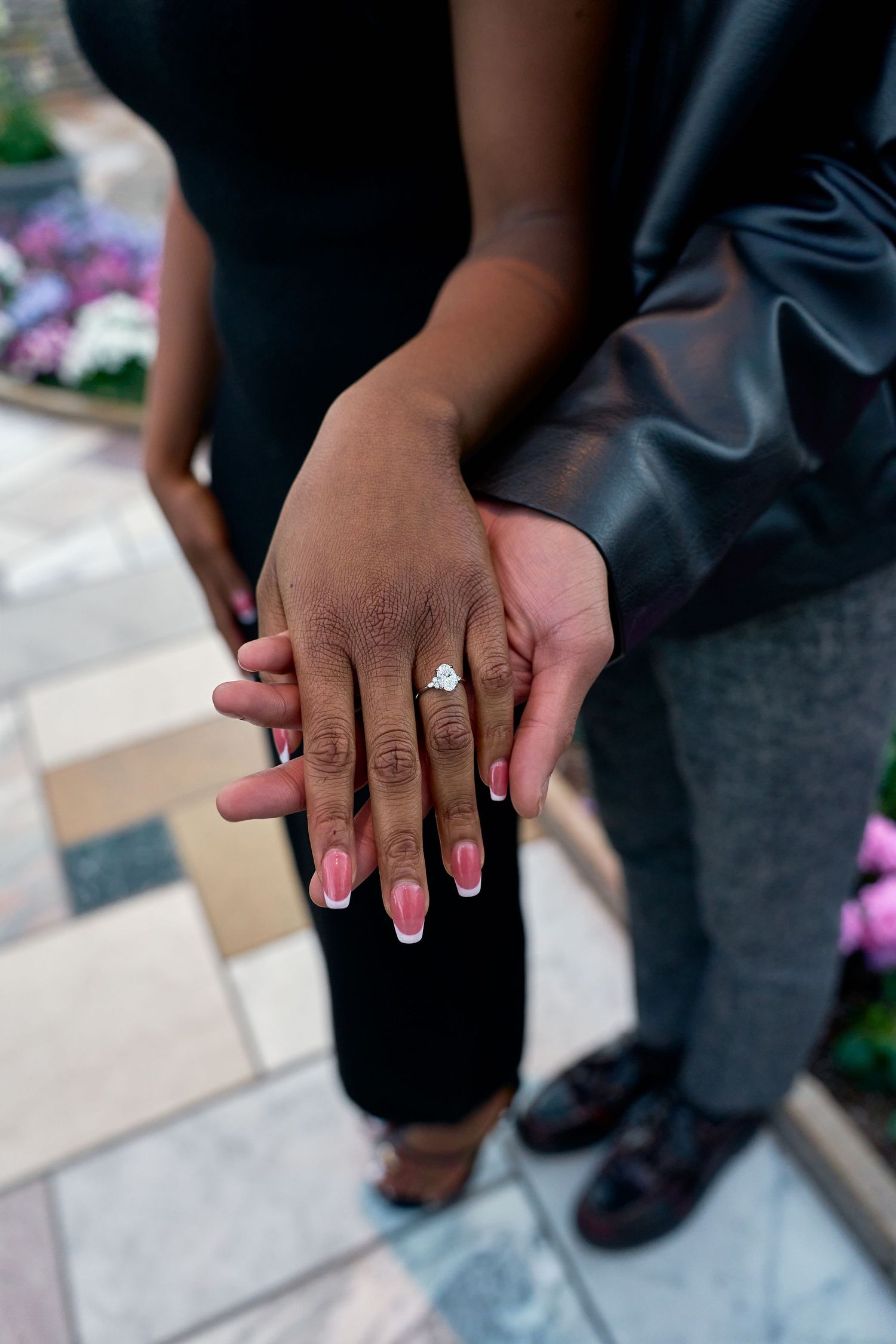 Close-up of engaged couples hands showing a sparkling diamond engagement ring with pink French manicure nails.
