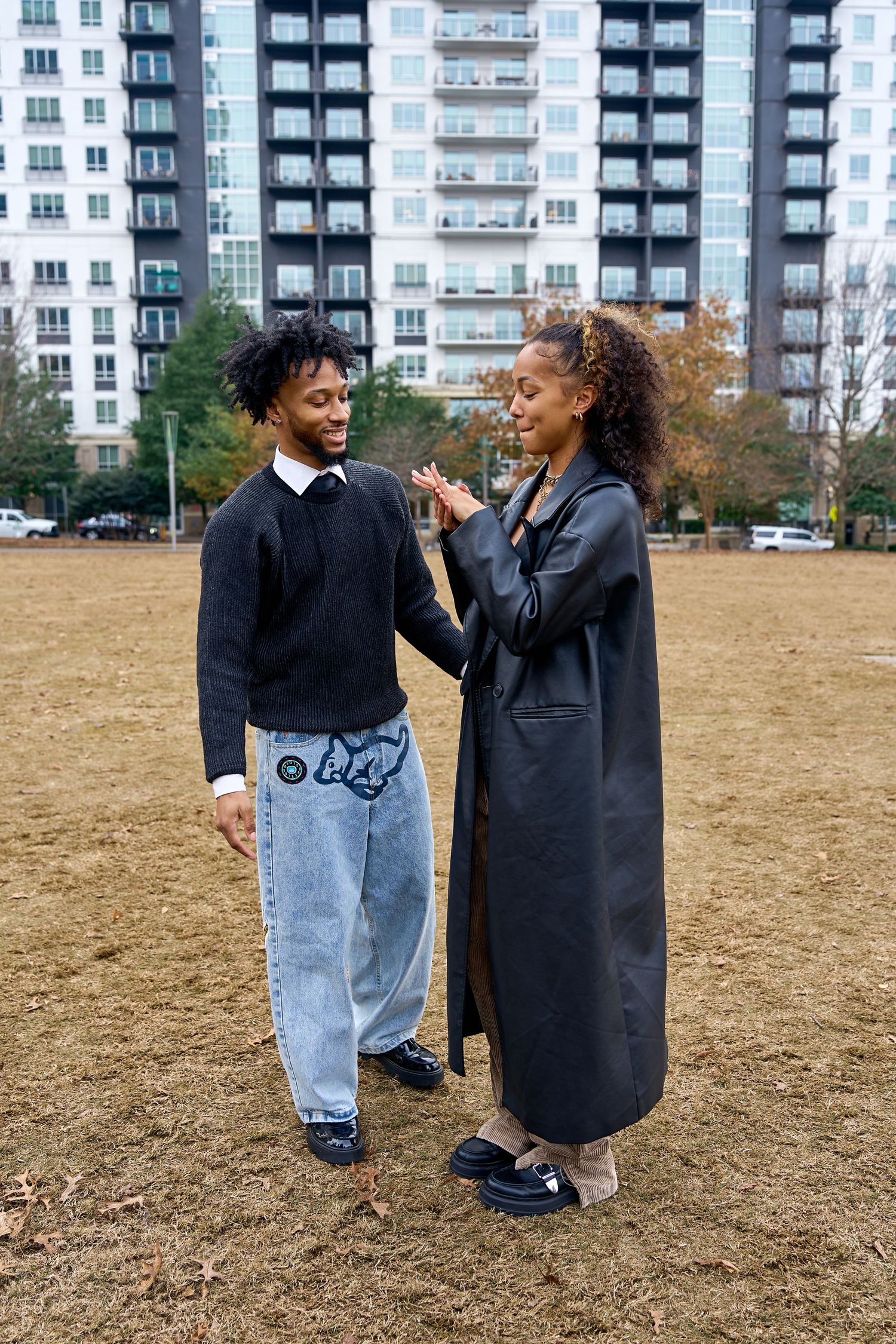 Two people laughing and interacting in a casual outdoor setting with apartment buildings in the background. NC Proposal Photographer.